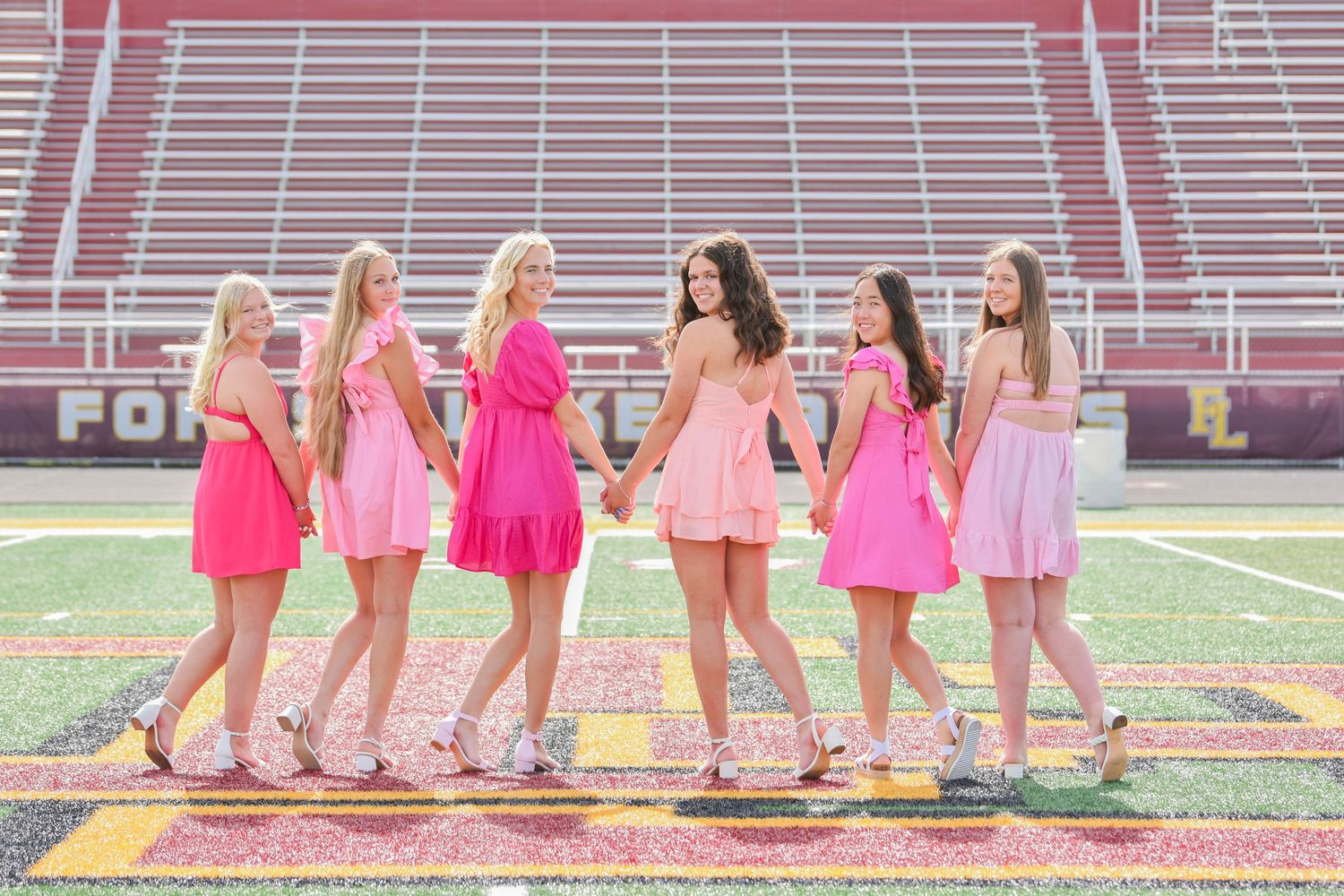 Group wearing pink dresses sitting on stadium bleachers.