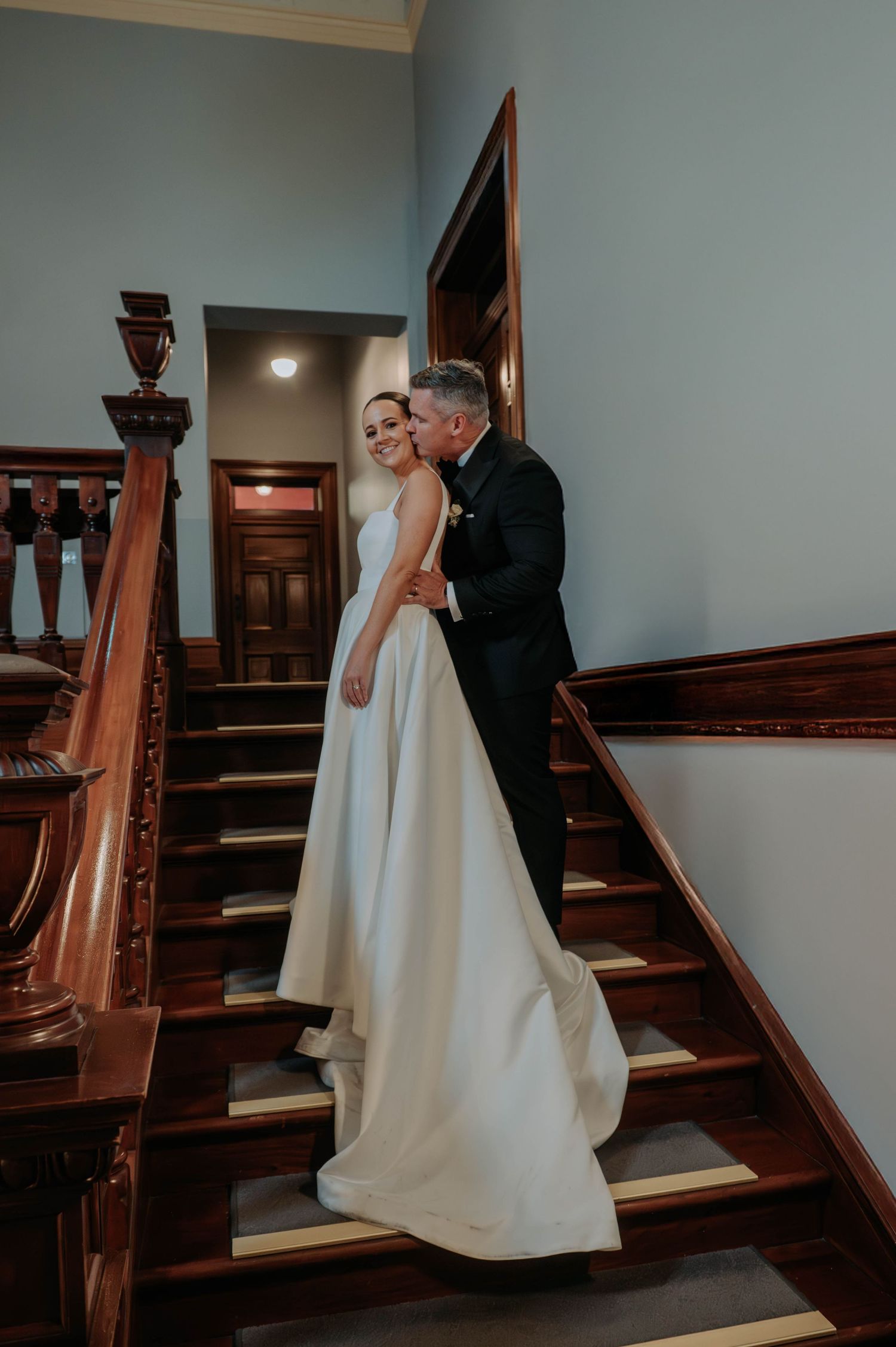 A couple poses together in an elegant wedding reception venue with black chairs and candlelit tables.