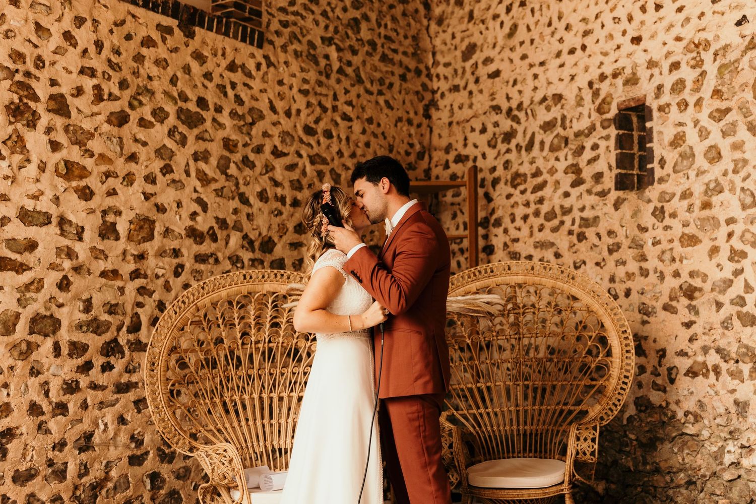 A romantic wedding moment captured in front of a stone wall with a vintage peacock chair.