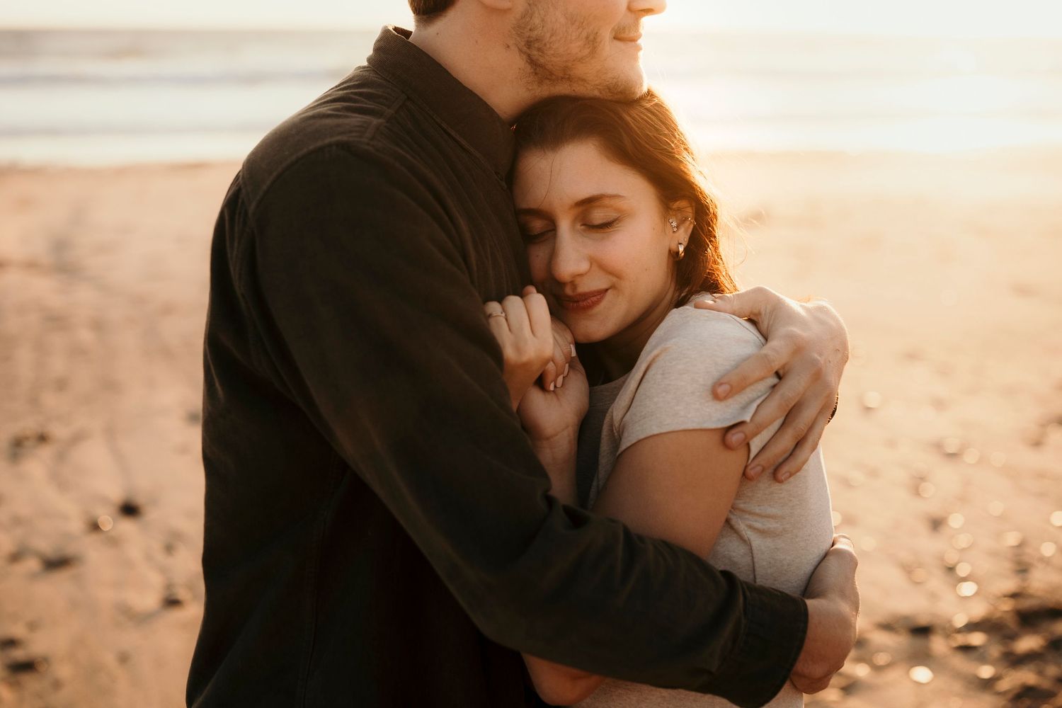 A tender embrace between a couple on a beach during golden hour.