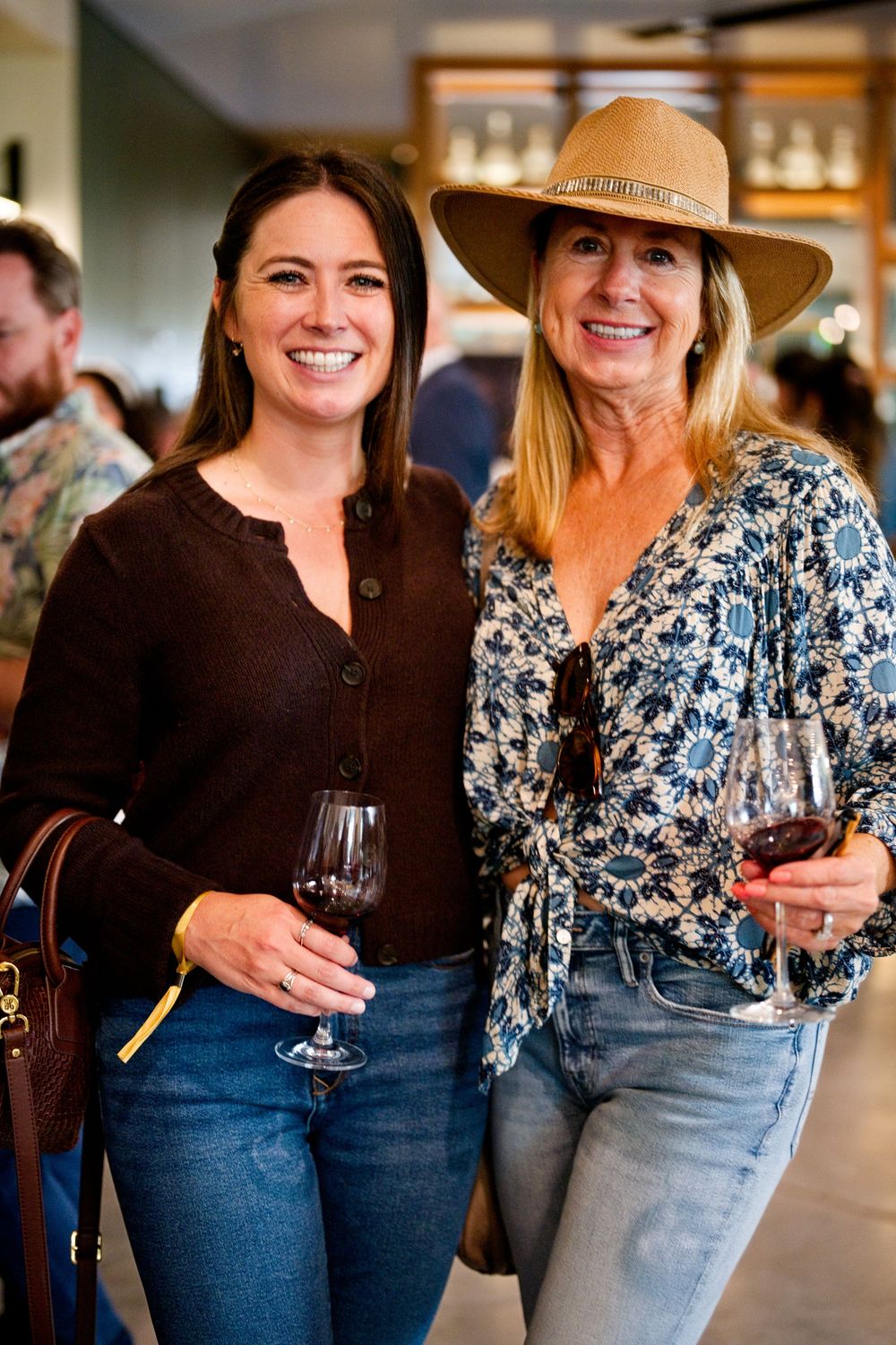 Two friends enjoy wine at a tasting event at CIA Copia, Napa Valley—one in a brown top, the other in a floral print with a hat.
