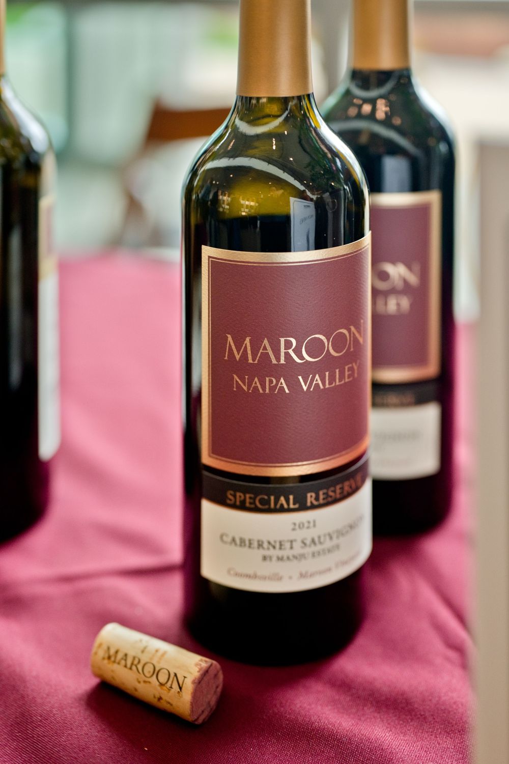 A bottle of Maroon Napa Valley Special Reserve Cabernet Sauvignon wine on a burgundy tablecloth with a cork.