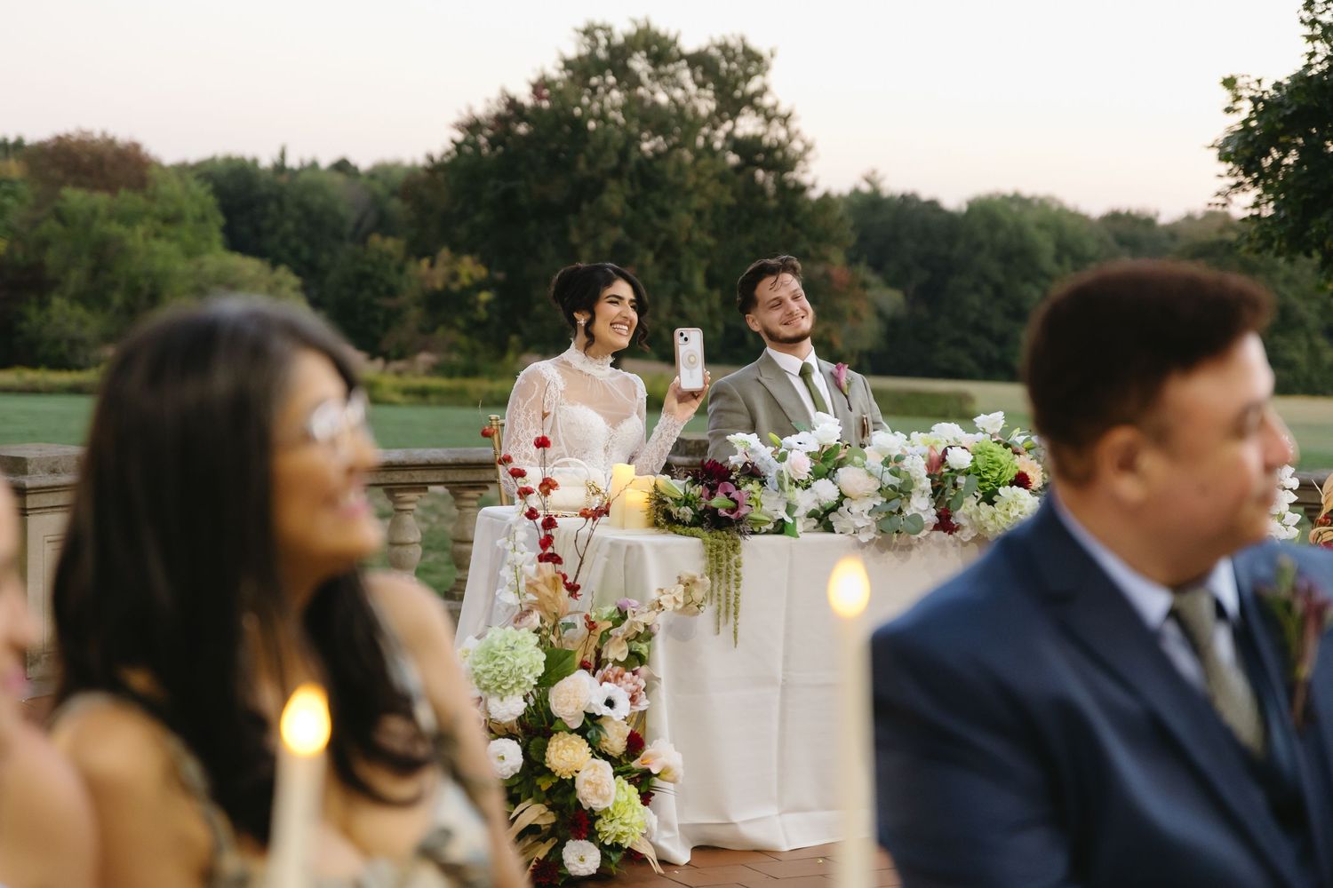 Wedding guests enjoying a reception at an outdoor venue with elegant table settings and floral arrangements.