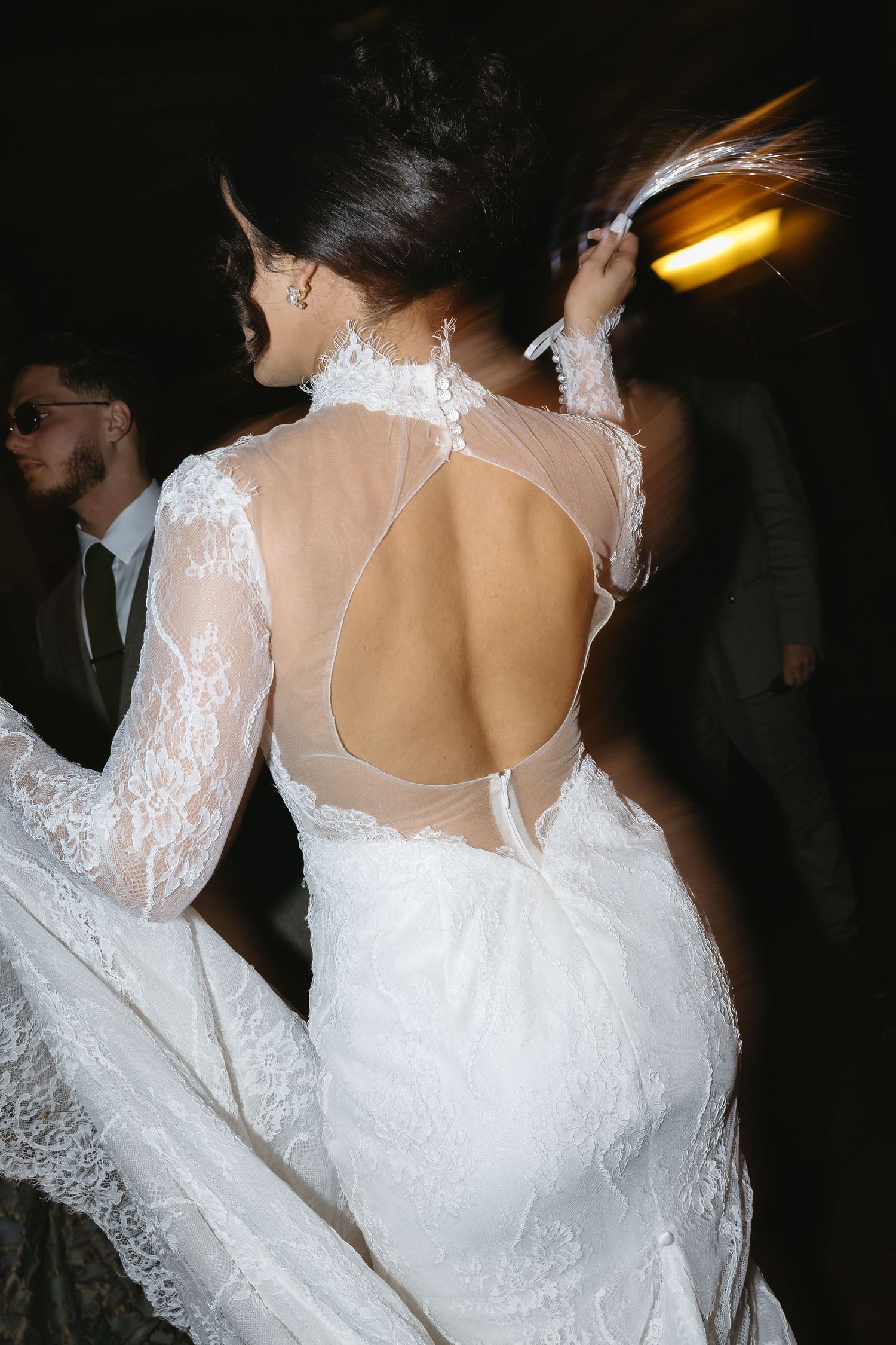 A bride wearing a white lace wedding dress with an open back design shows off the elegant details of her gown.