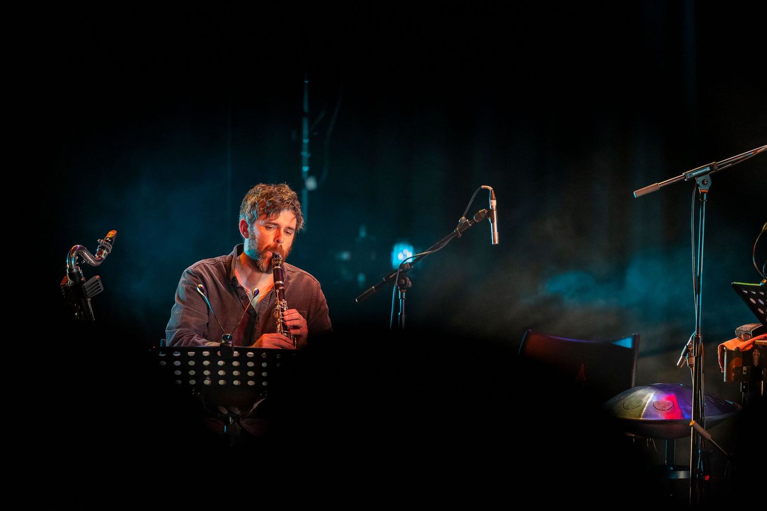 A musician performs on a dimly lit stage with blue atmospheric lighting and a microphone stand visible in the background.