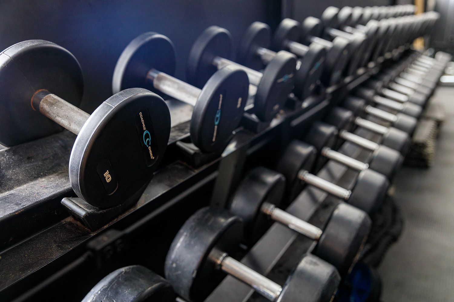 Row of black dumbbells arranged neatly on a metal rack in a gym setting. live event photography st louis.