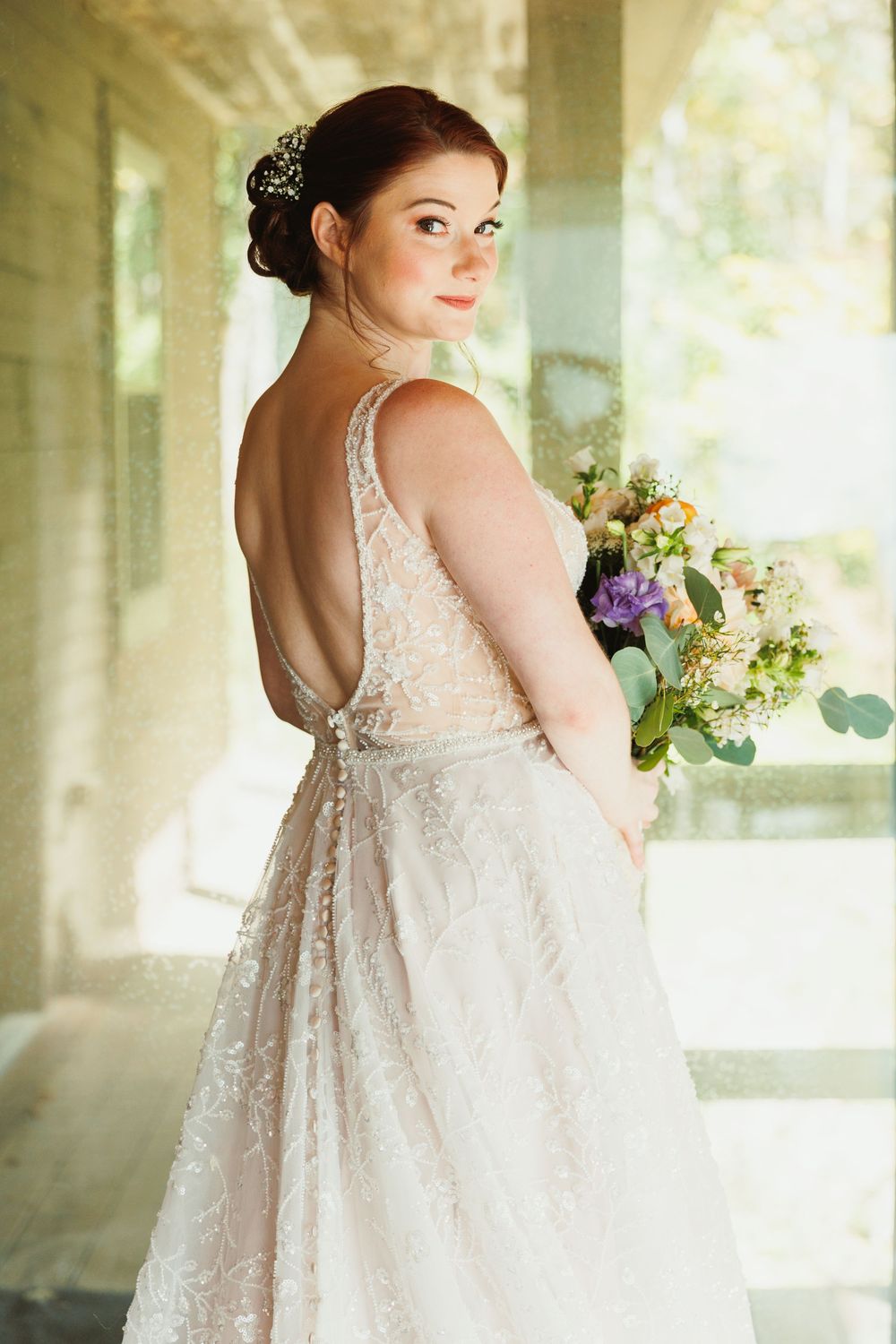 An elegant bridal portrait showing the back detail of a lace wedding gown with a bouquet.