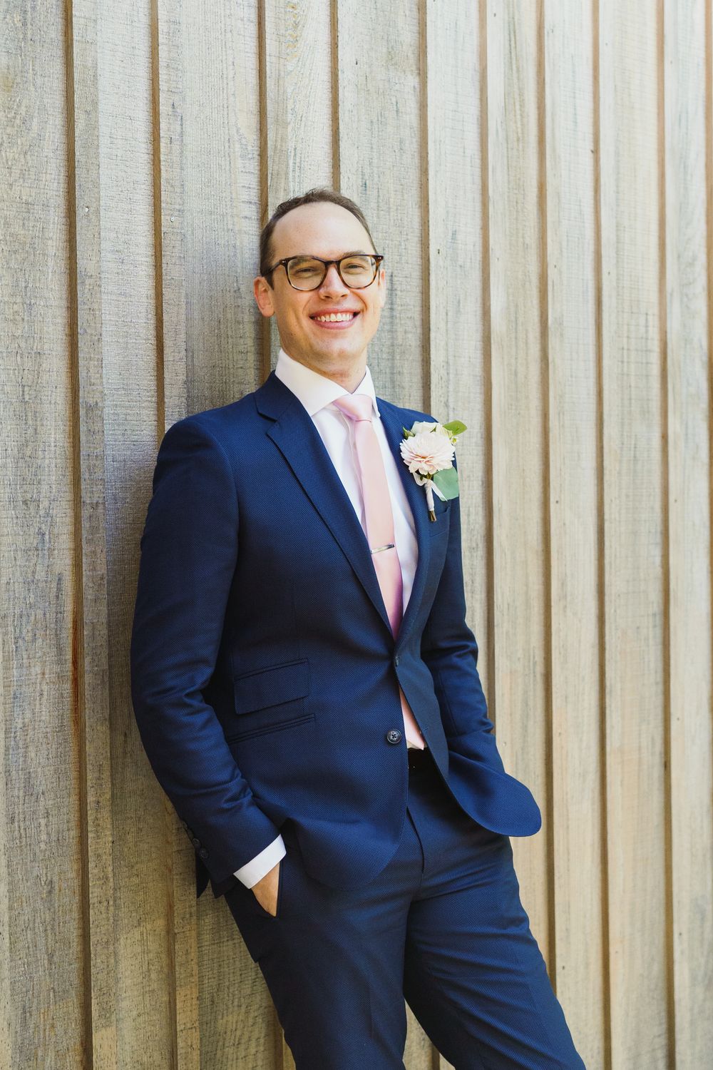 A groom in a fitted navy suit and pink tie poses against a striped wall.