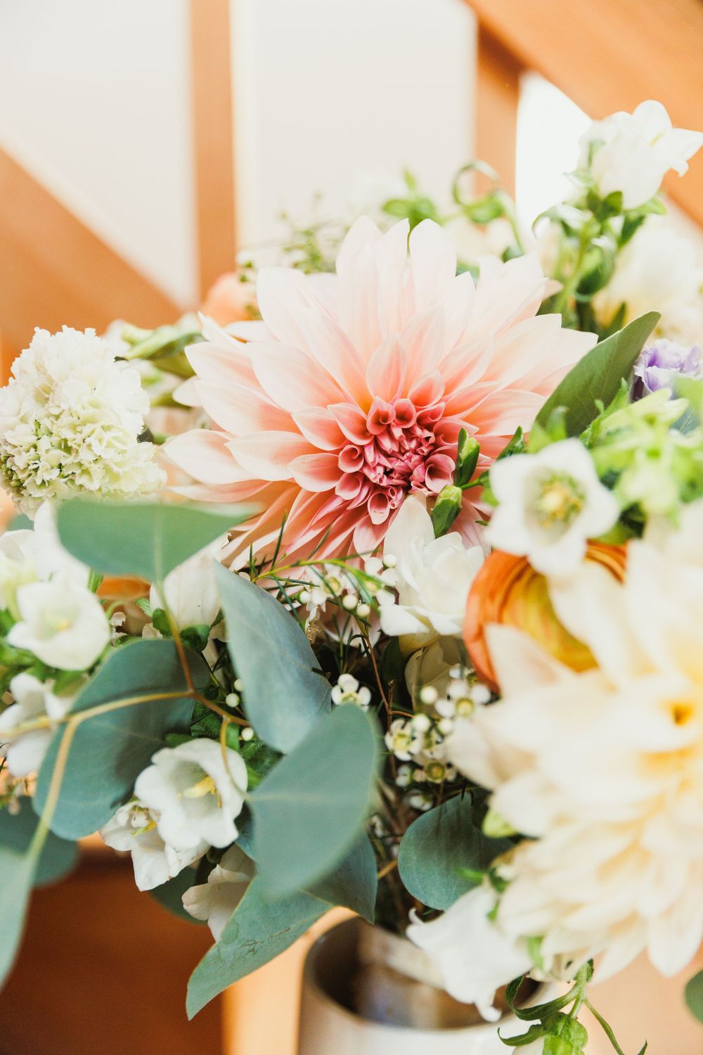 Close-up of a wedding flower arrangement with coral dahlias, white blooms, and eucalyptus.
