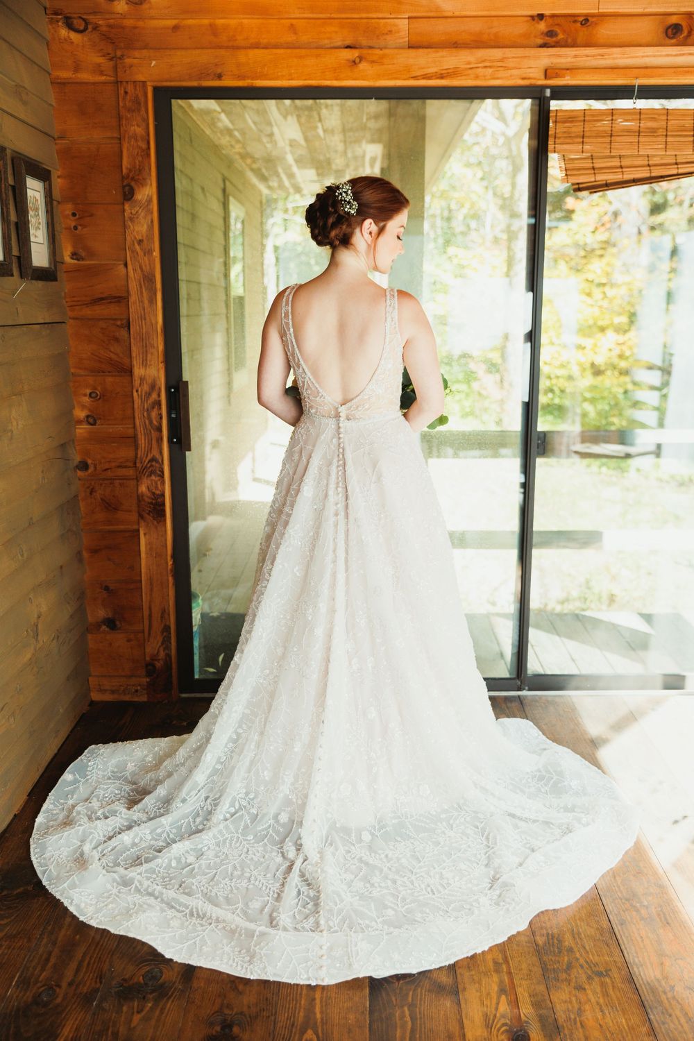 A stunning back view of a white lace wedding gown with a cathedral train on hardwood floors.