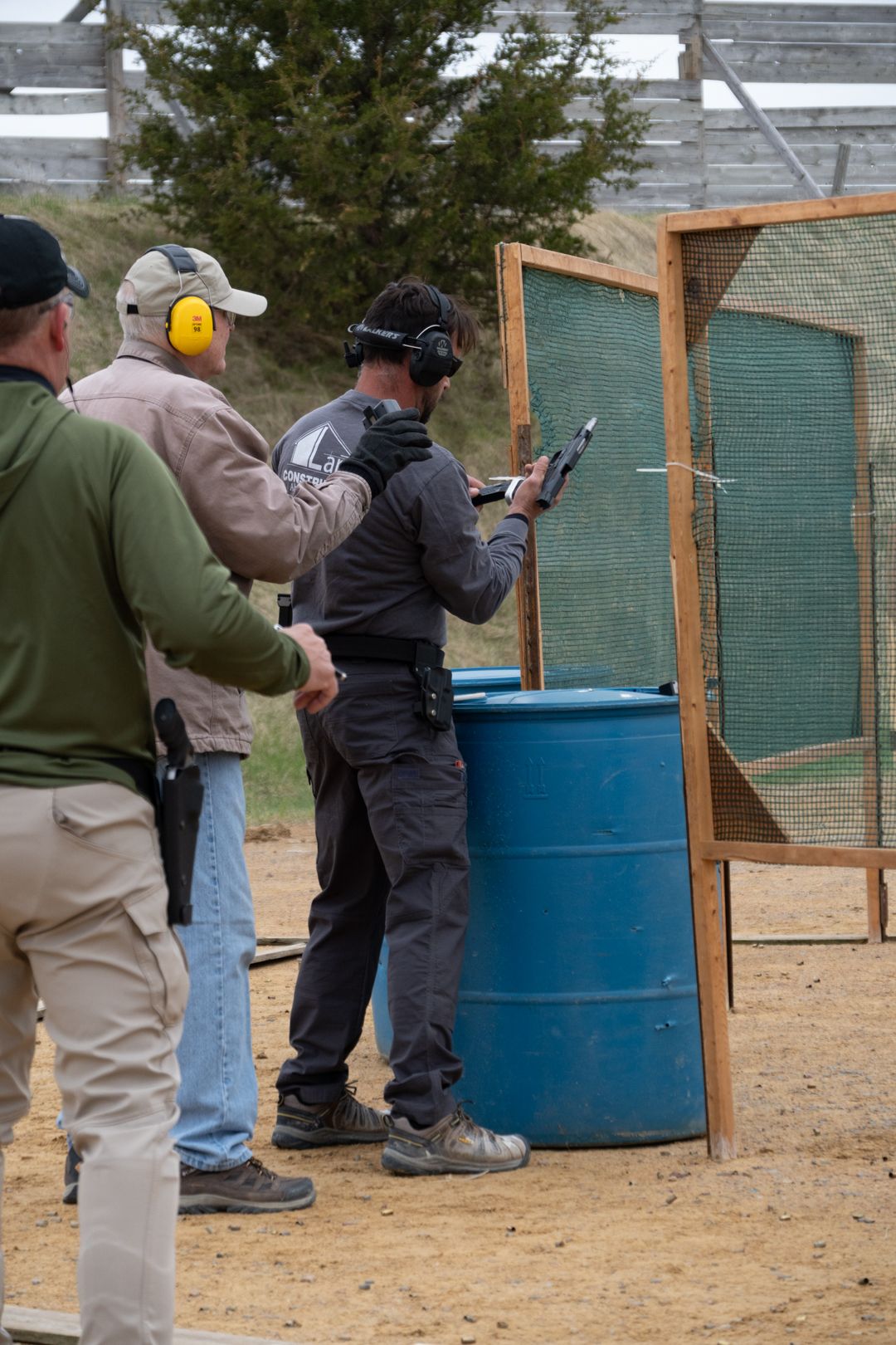 A group of people practicing shooting techniques at an outdoor firing range with firearms and safety gear.
