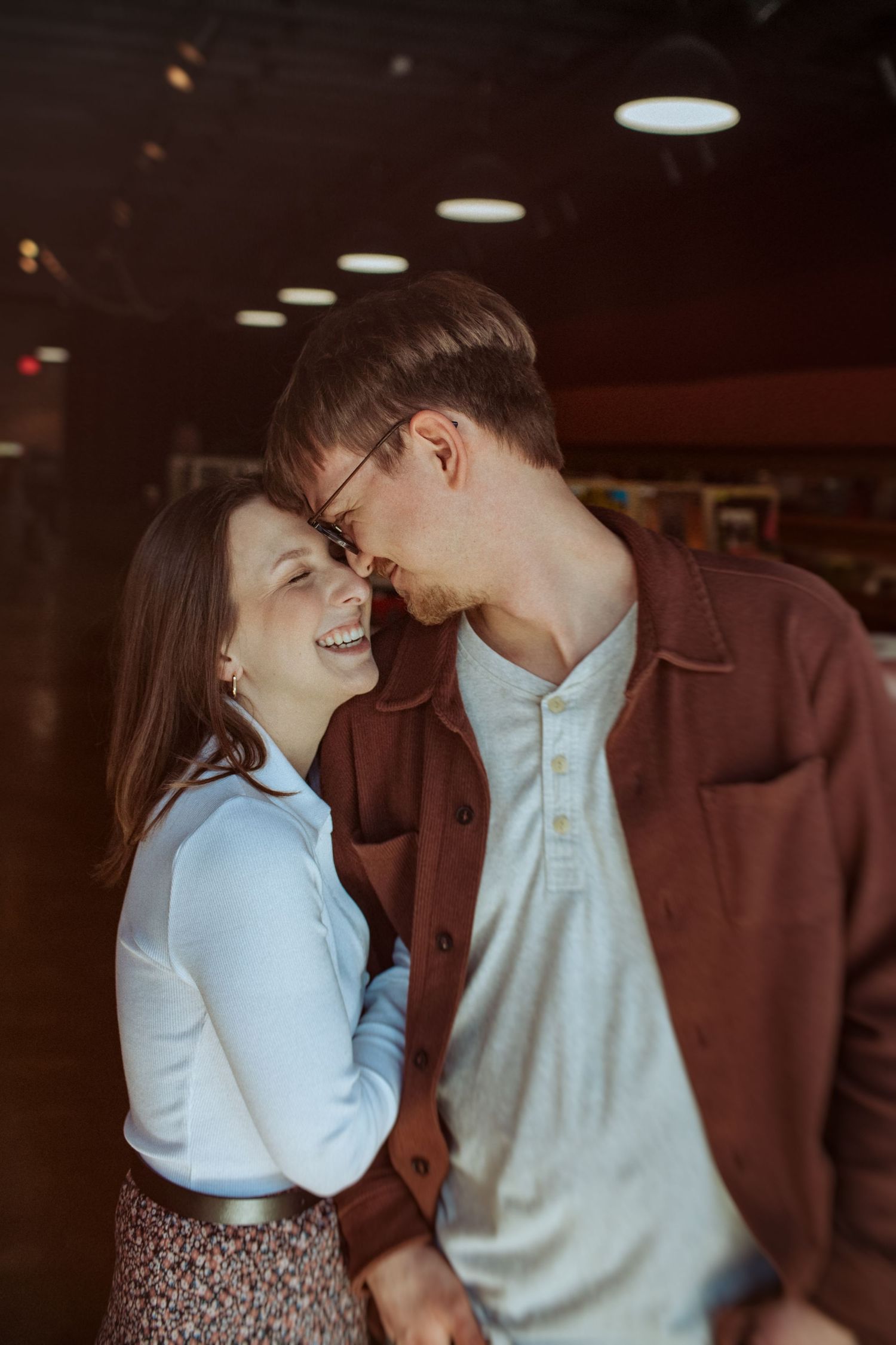 A romantic couple in casual attire shares tender moments together in a dimly lit indoor setting. Indianapolis, Indiana engagement session.