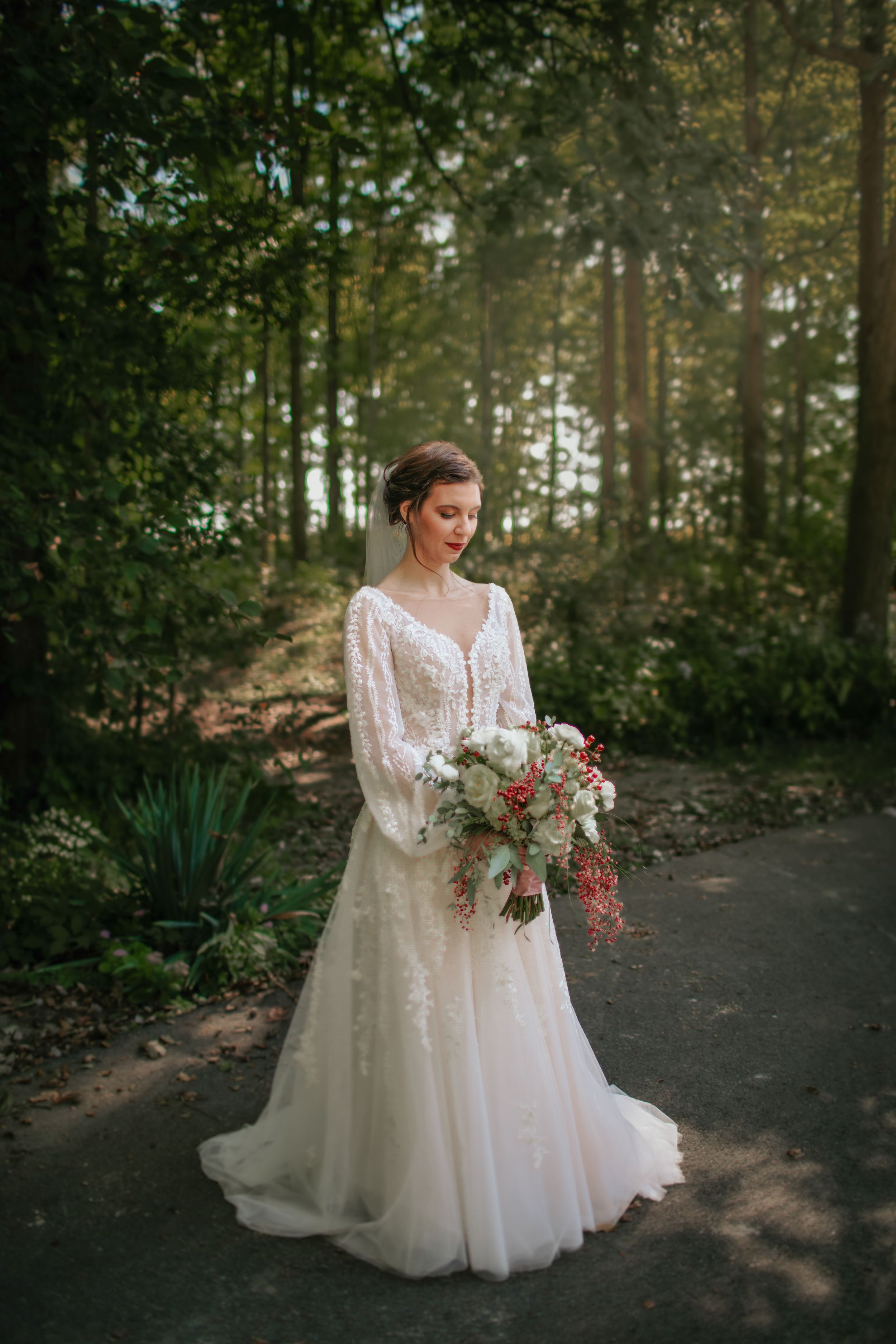 Elegant bridal portrait in a wooded setting with a lace gown and floral bouquet.