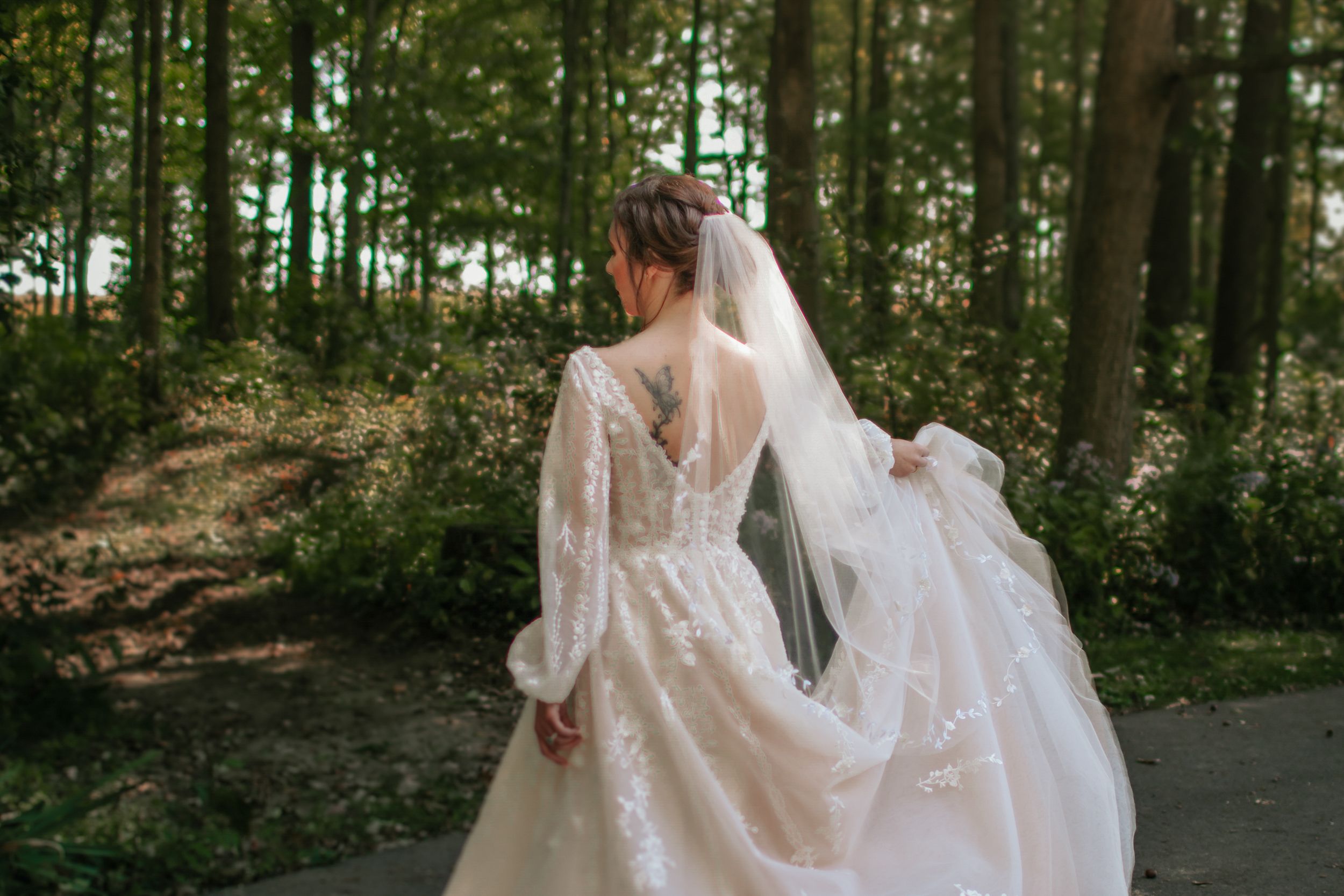 Bride twirling in a flowing lace gown among forest trees.