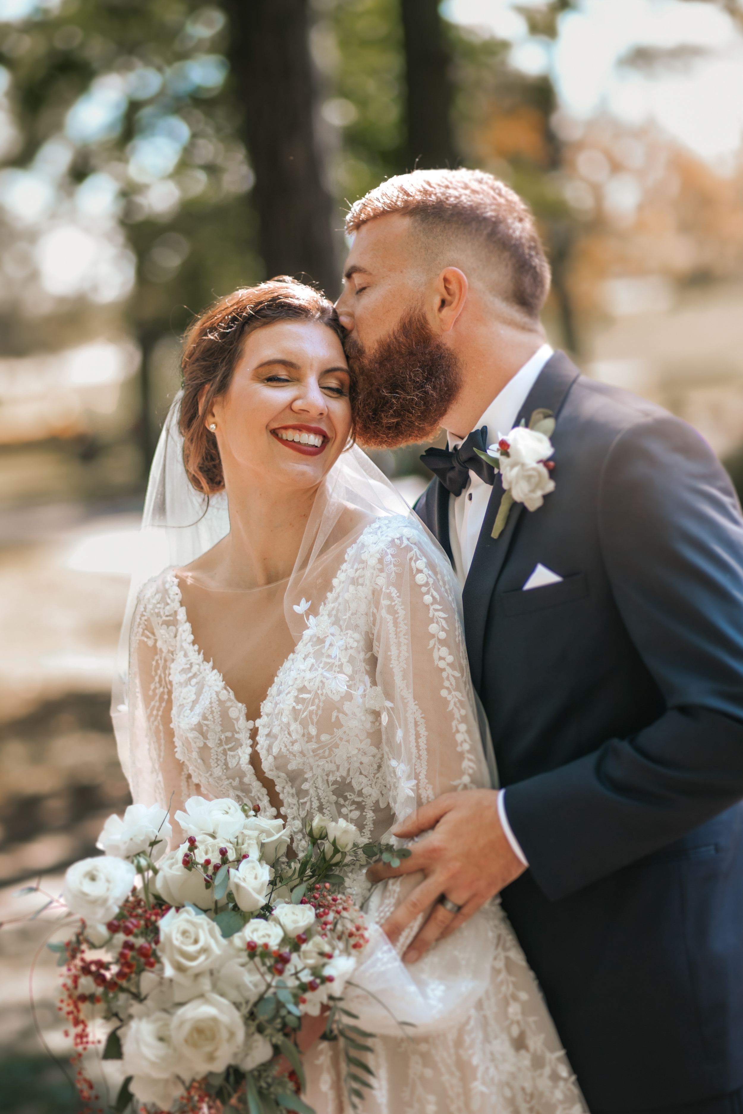Newlyweds share intimate moment outdoors with bride holding white and blush floral bouquet.