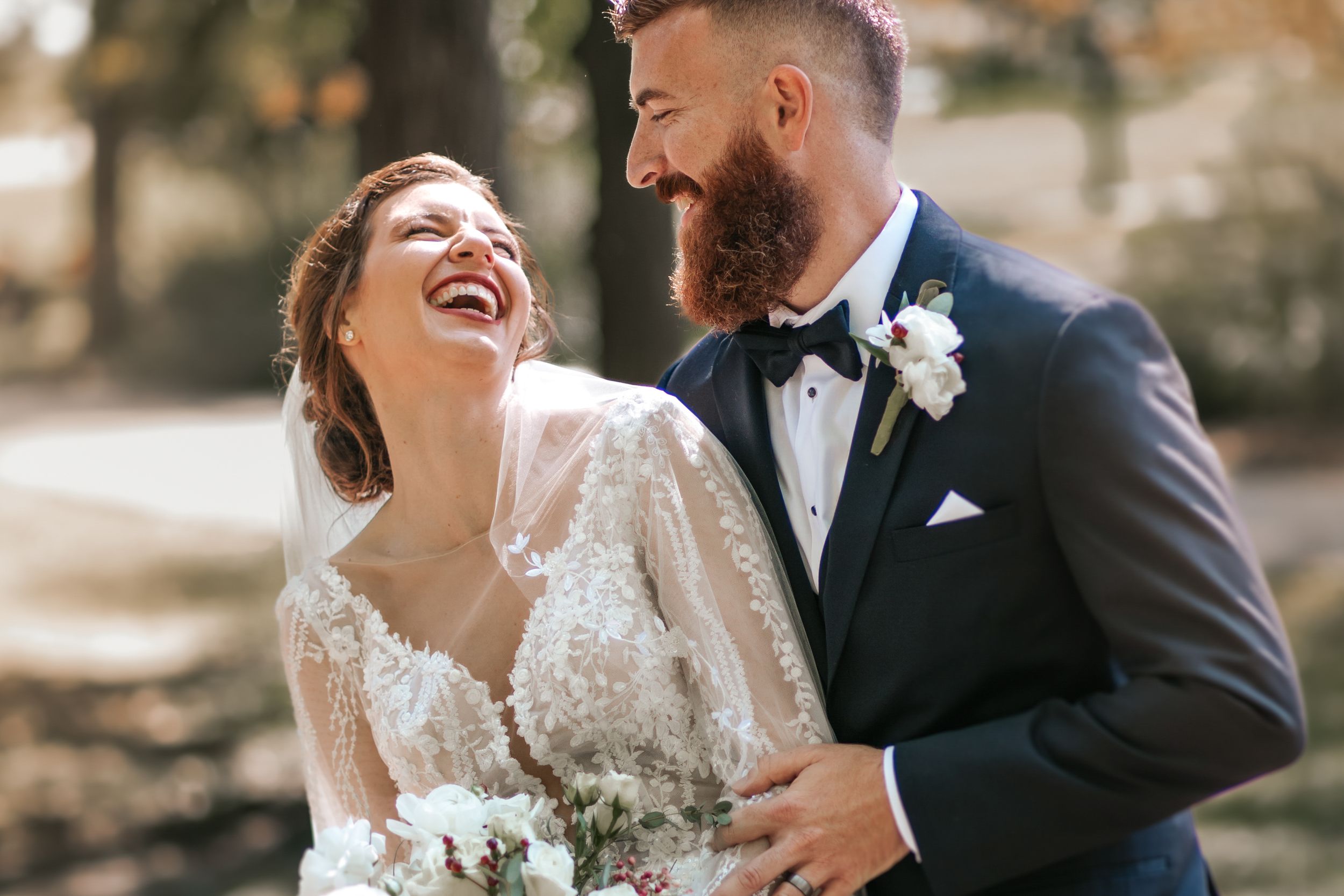 Joyful wedding couple laughing together during outdoor photo session.