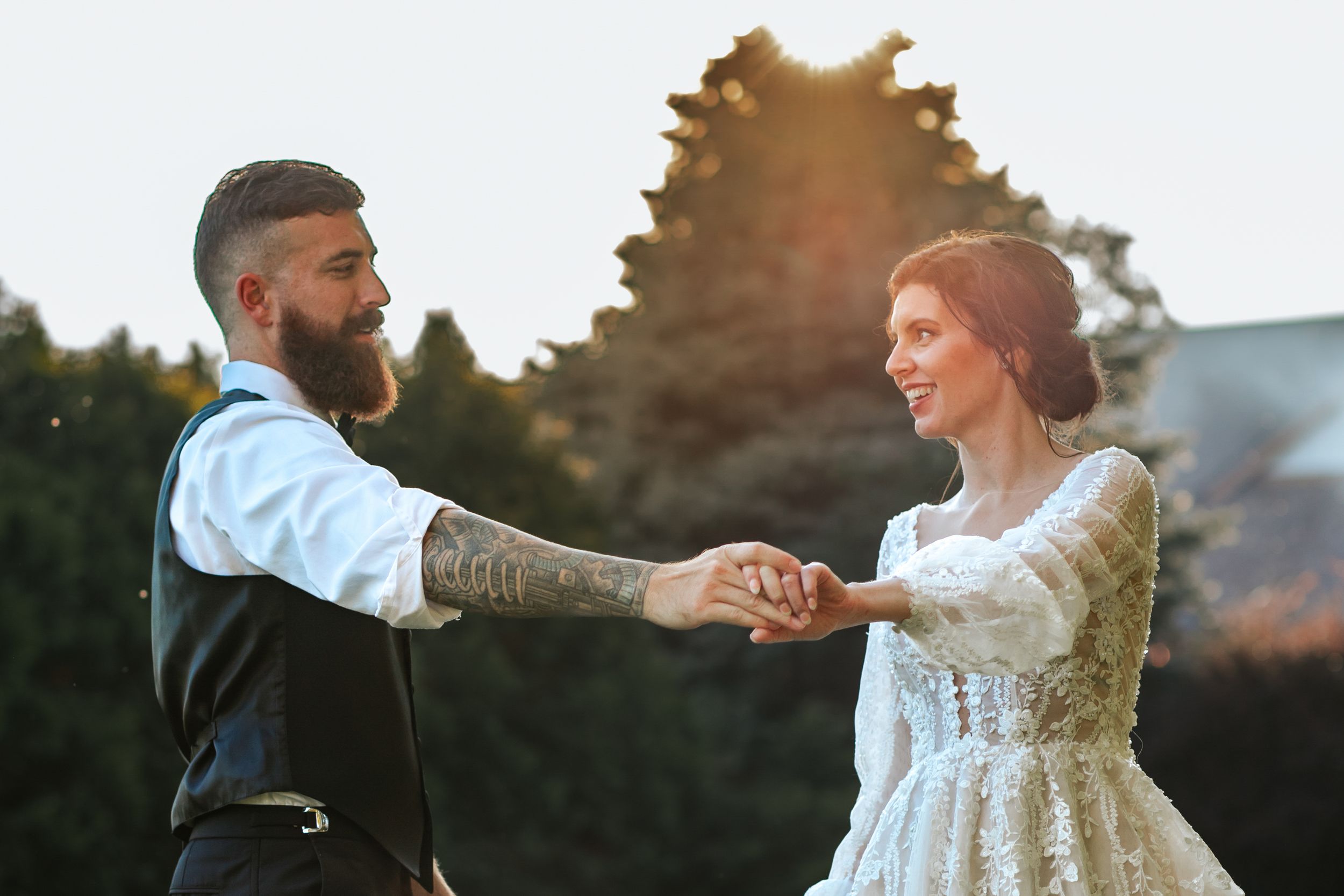 Wedding couple dances together in a grassy field at sunset.