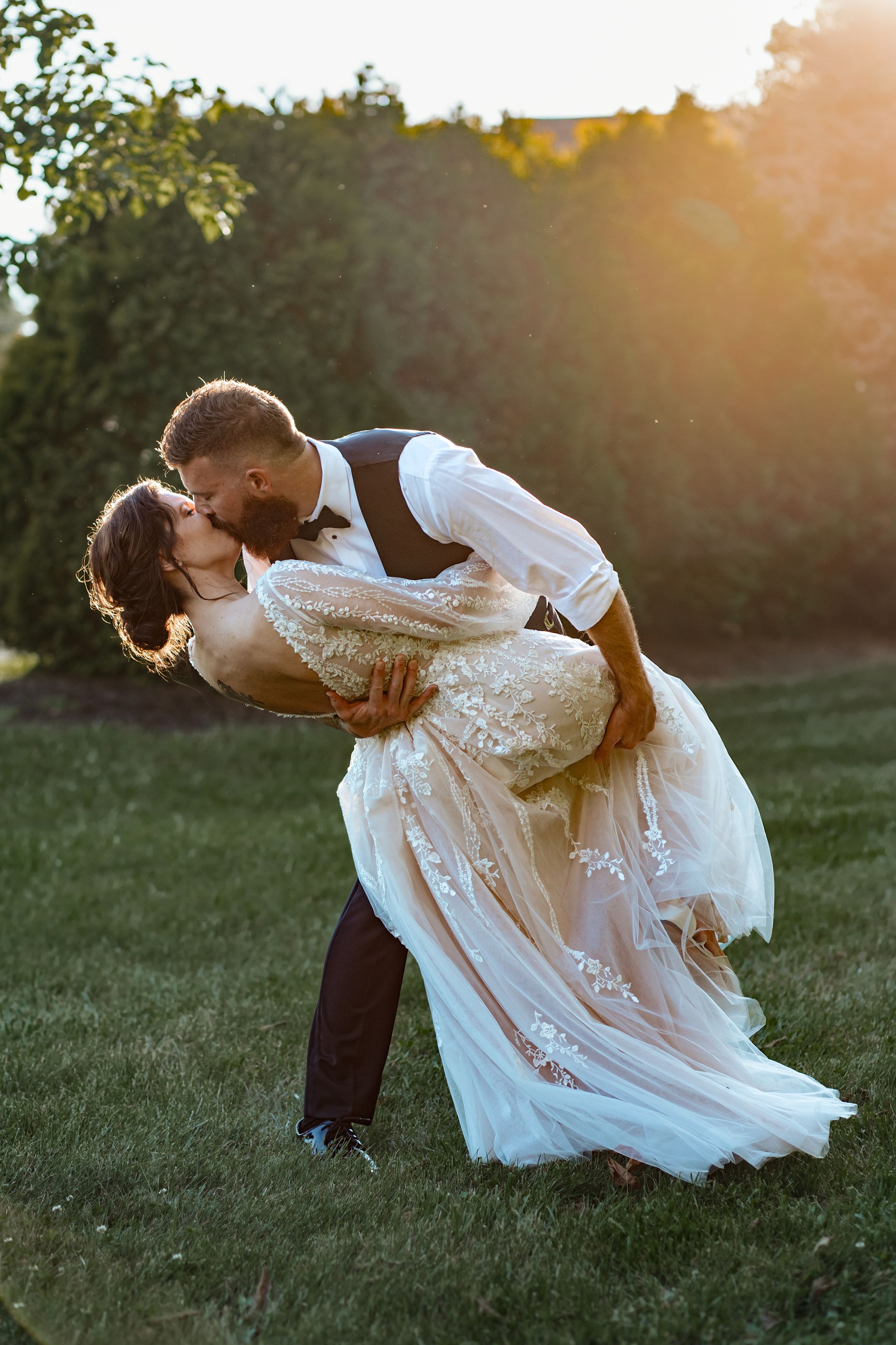 Dramatic dip pose during outdoor wedding photoshoot at golden hour.