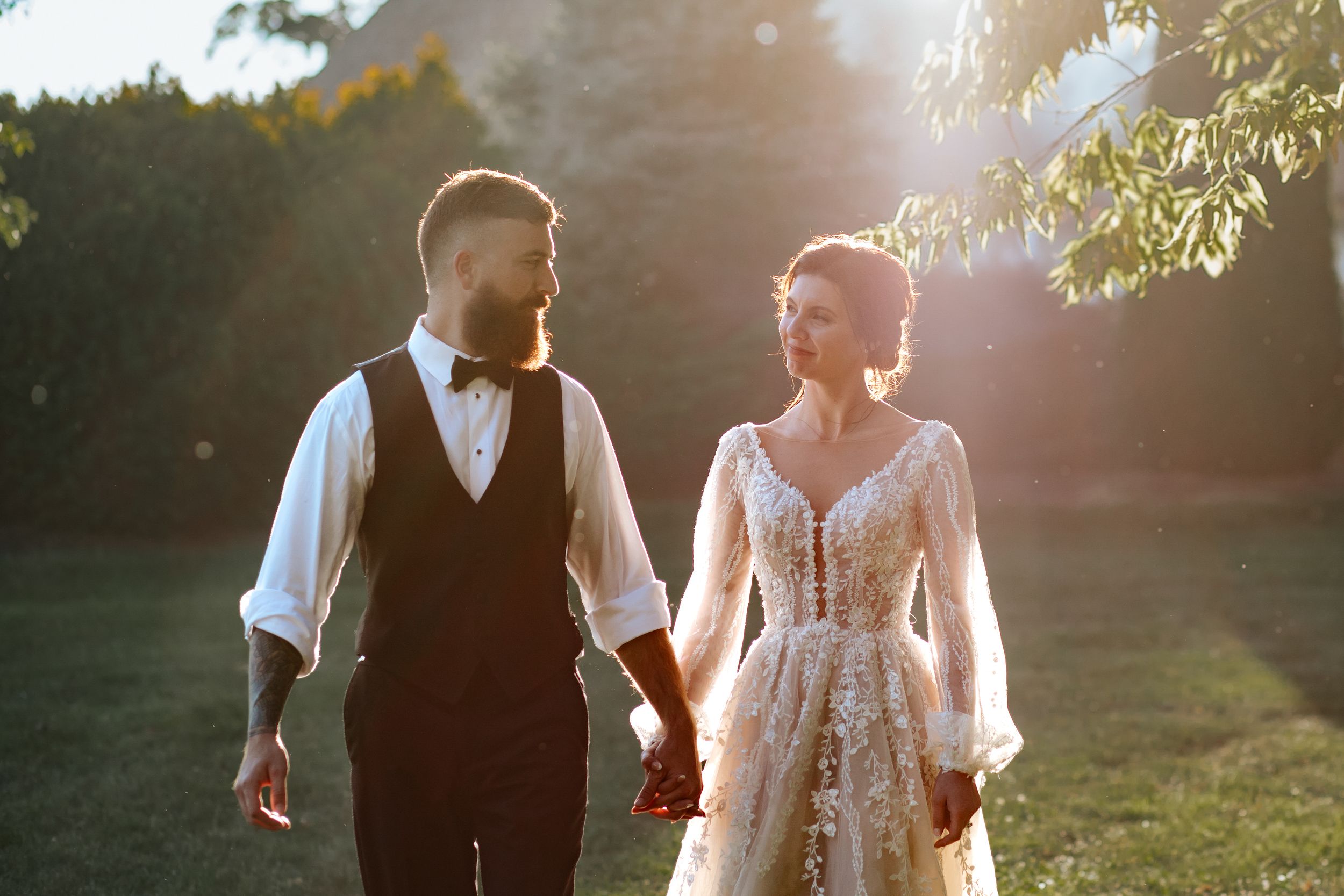 Newlyweds walk hand in hand through a sunlit garden during their wedding celebration.