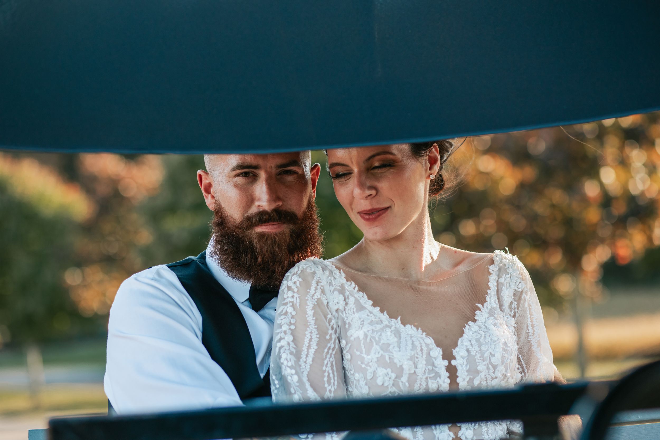 Close up wedding portrait captured through a reflective surface showing formal attire and intimate moment.
