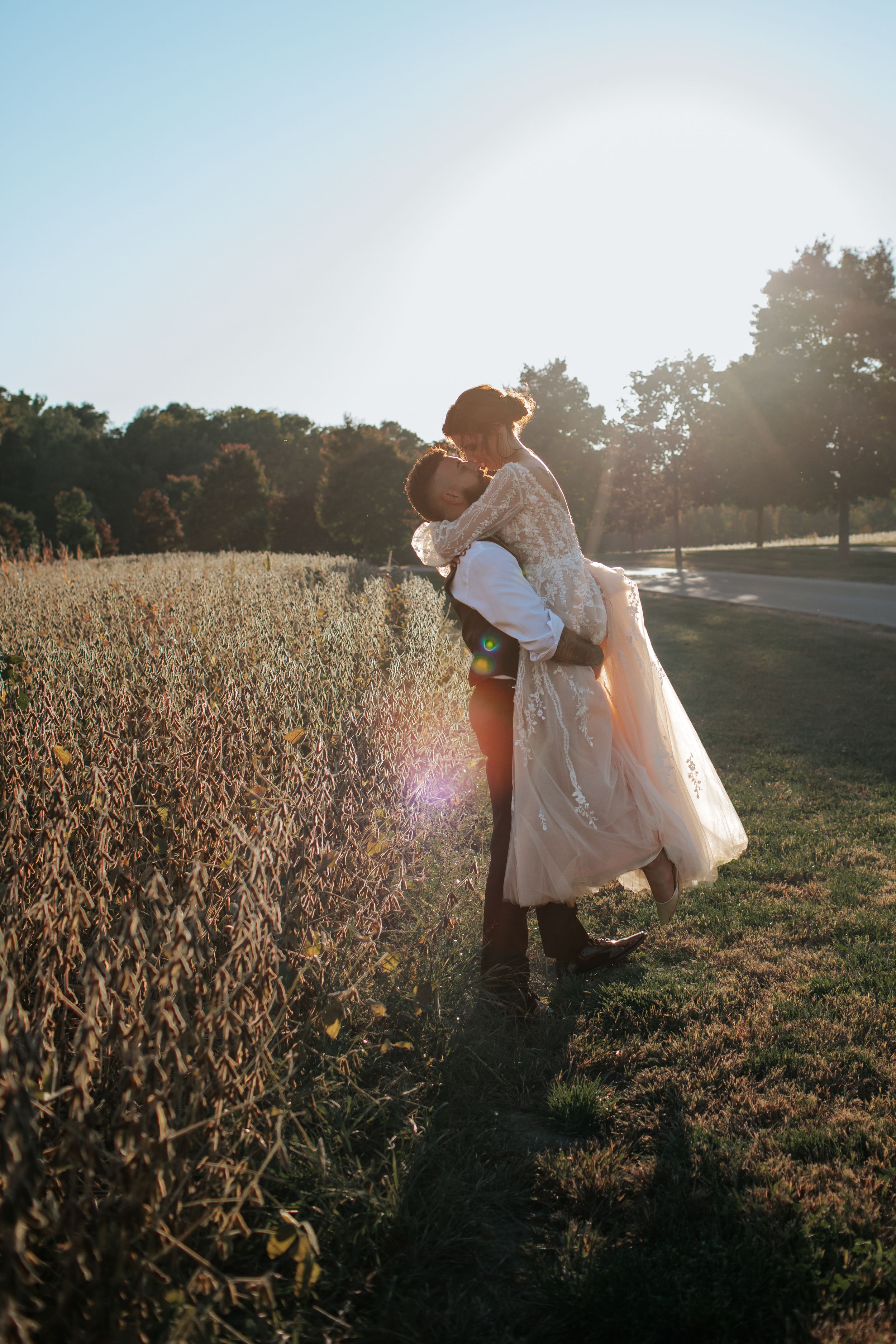 Romantic sunset wedding photo captures couple in intimate embrace beside tall grasses.