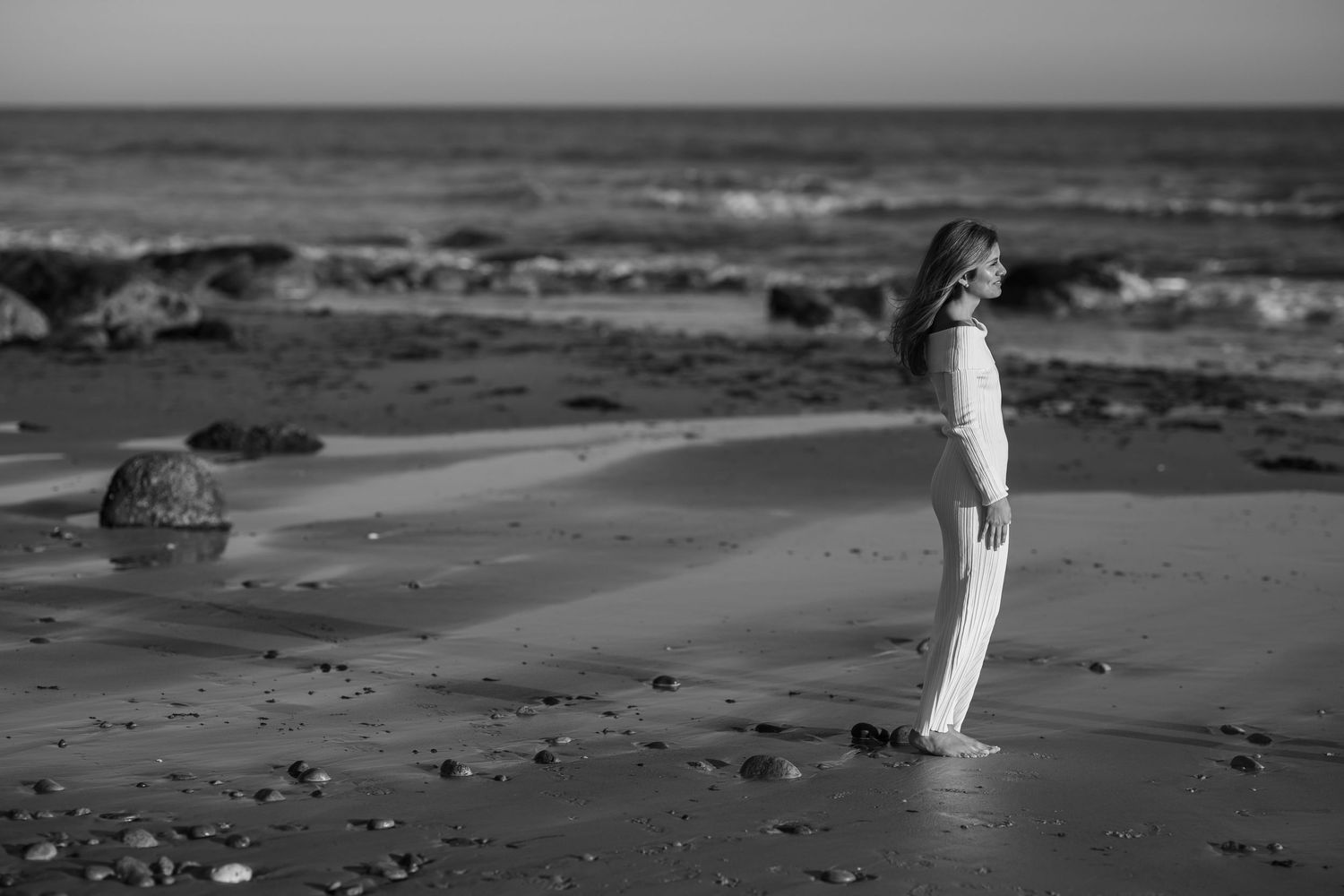 Black and white photo of a child standing alone on a sandy beach near the ocean.