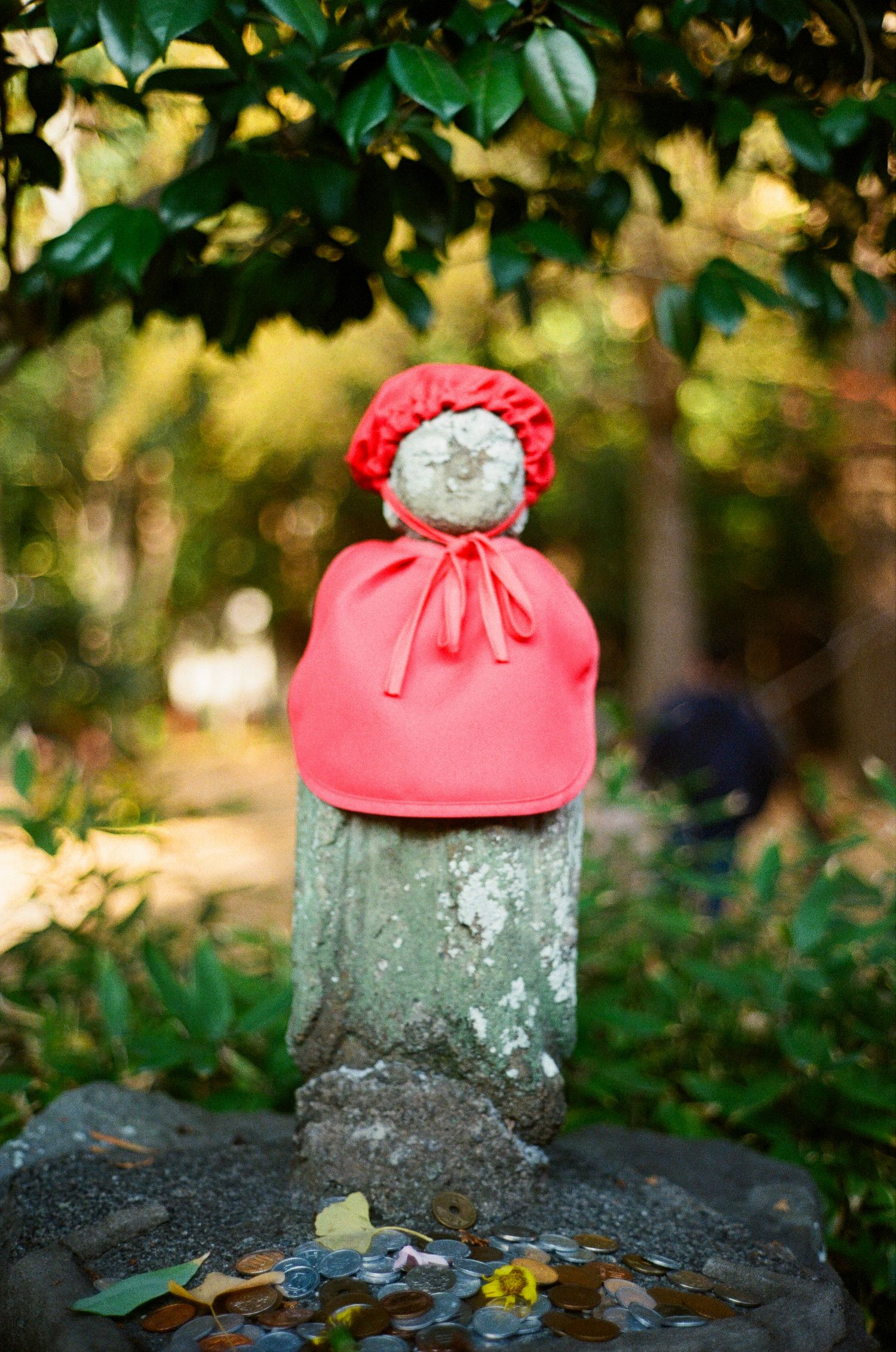 A visitor in a red coat bows in front of the Great Buddha statue at Kamakura, Japan against a blue sky.