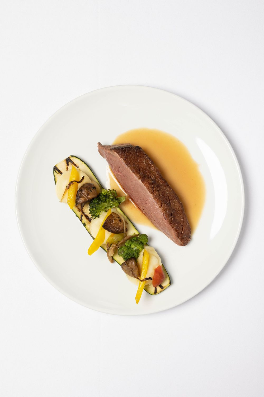 Four white plates with elegantly plated gourmet dishes featuring meat and vegetables in a minimalist presentation.