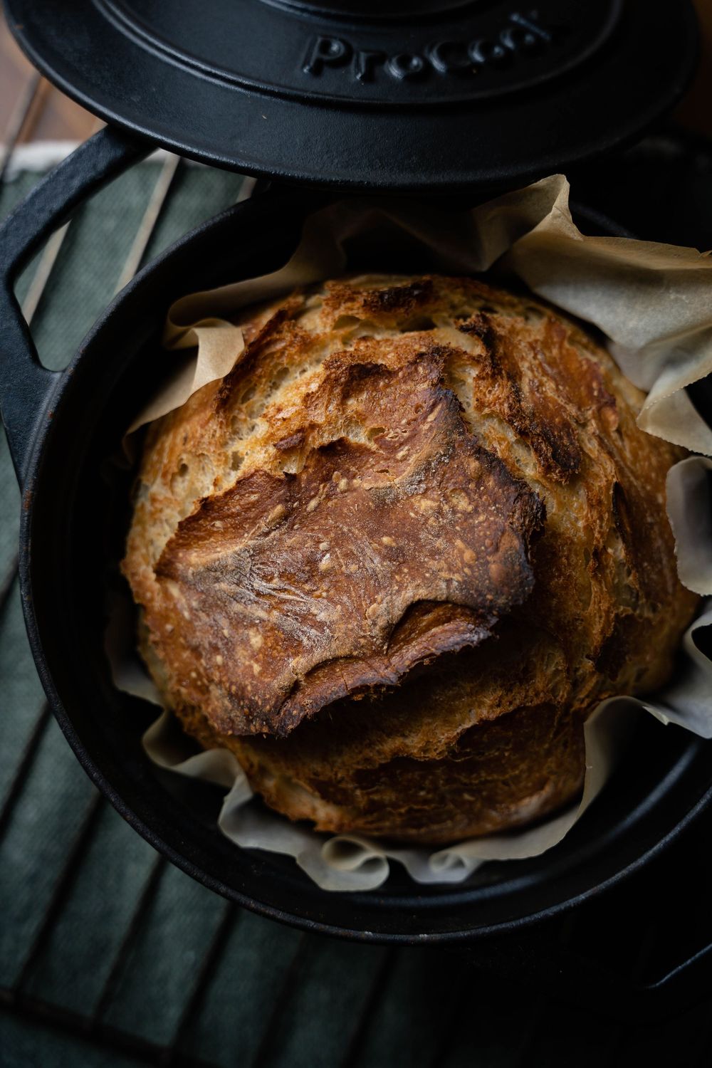 Rustic homemade sourdough bread with dark golden crust baking in cast iron Dutch oven with parchment paper.