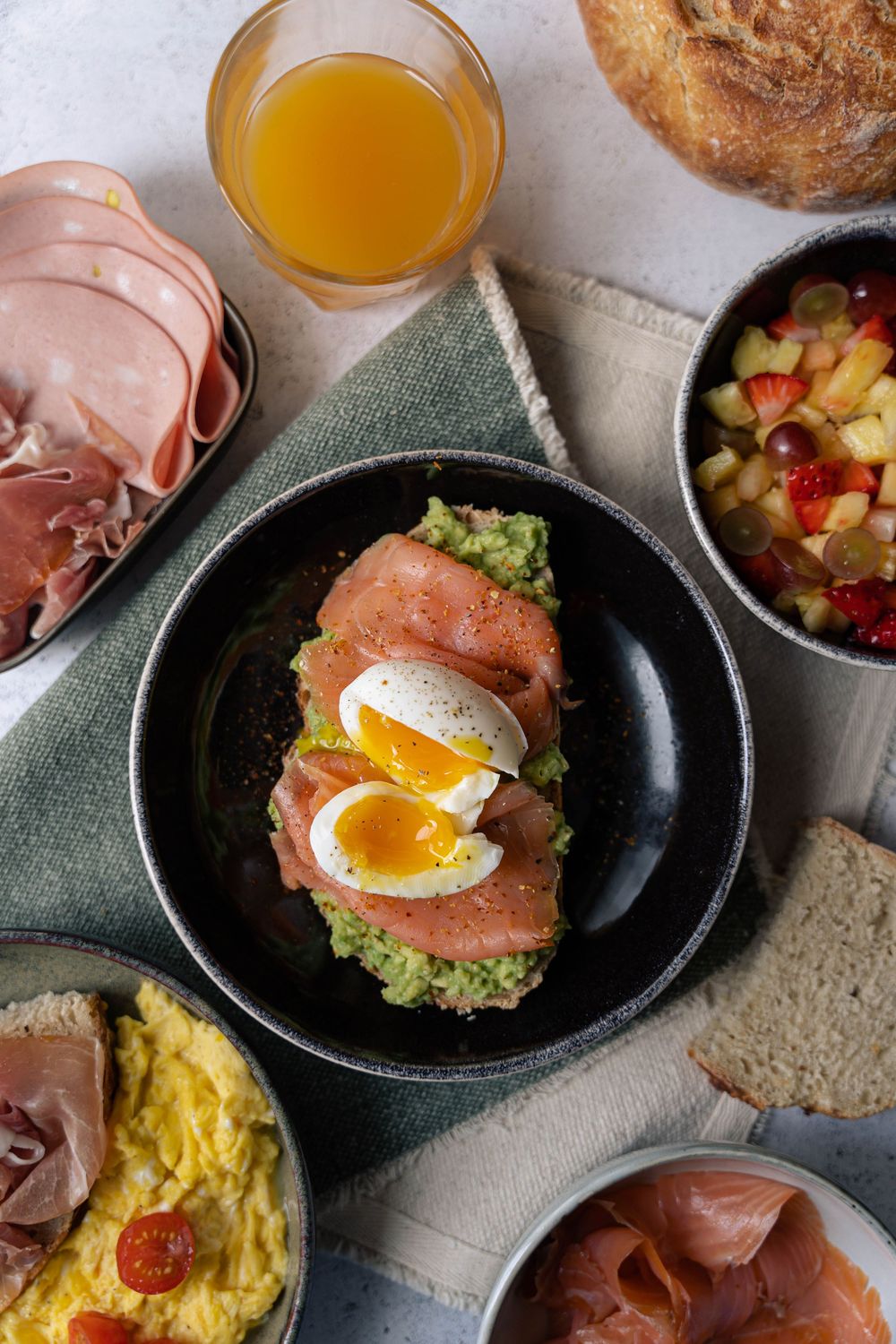 A sequence showing the assembly of eggs benedict with smoked salmon and avocado on plates with orange juice and toast.