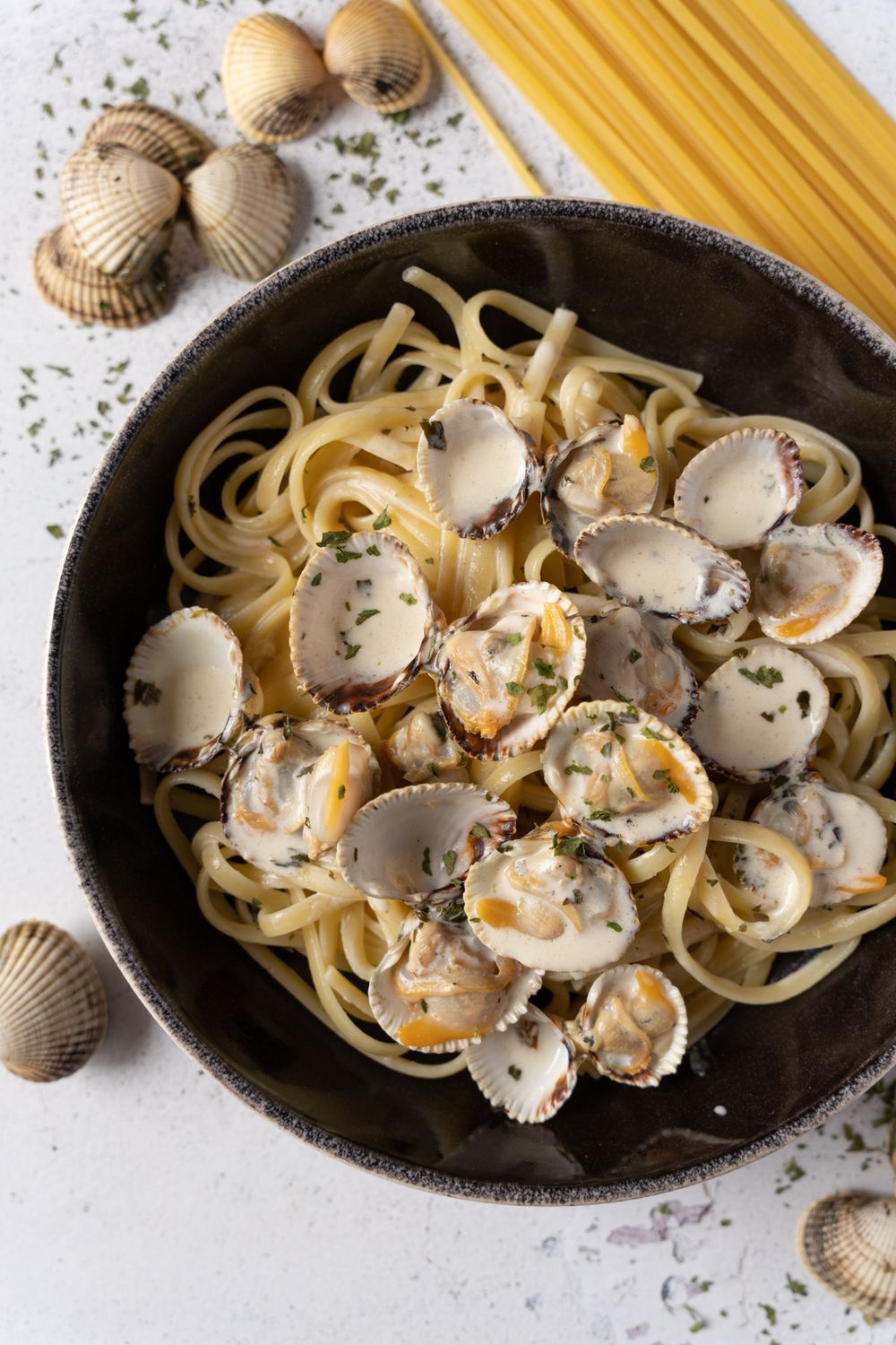 Fresh spaghetti with clams and herbs served in a black cast iron pan showing cooking progression in multiple stages.