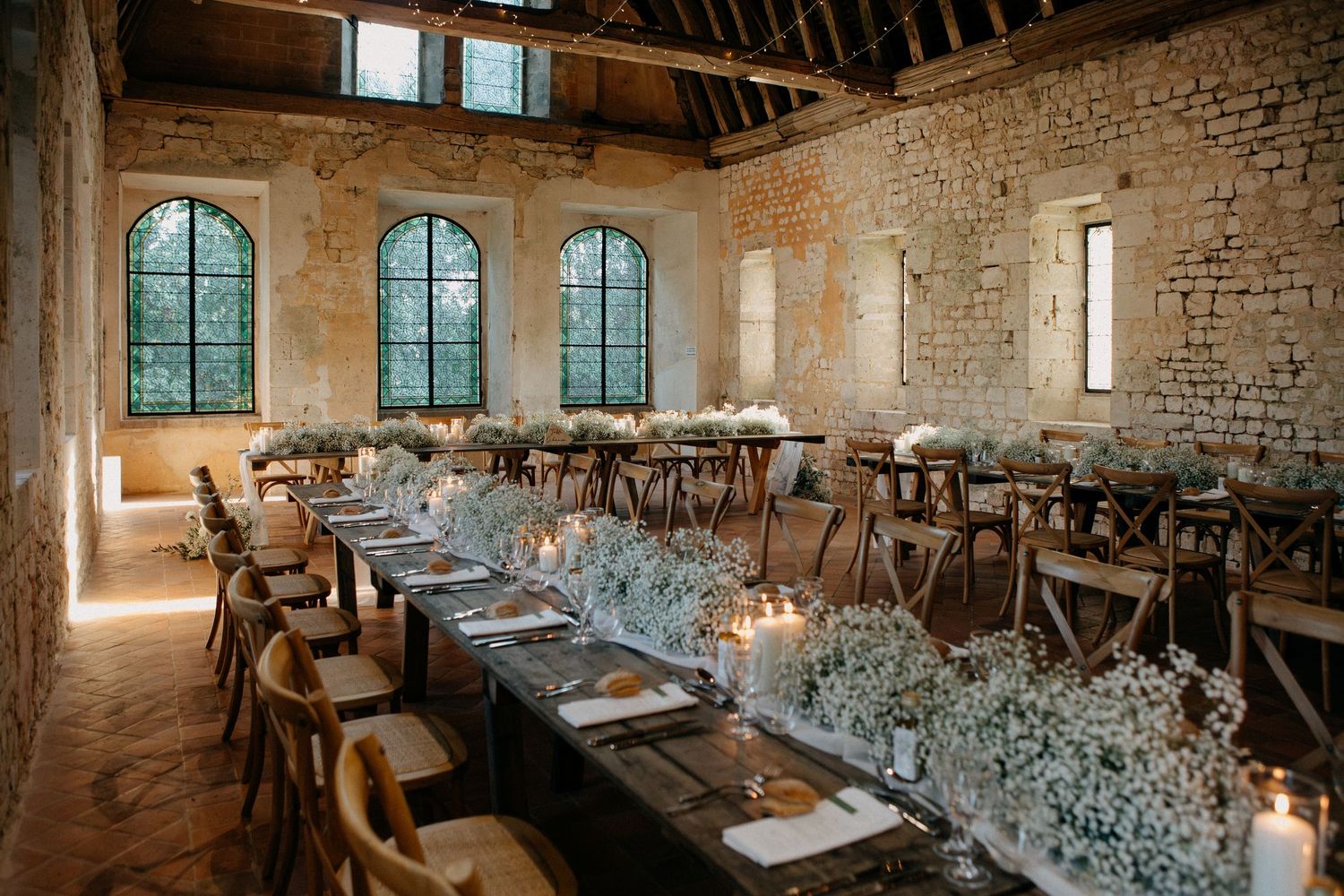 Rustic stone barn wedding reception with long wooden tables adorned with white floral centerpieces.