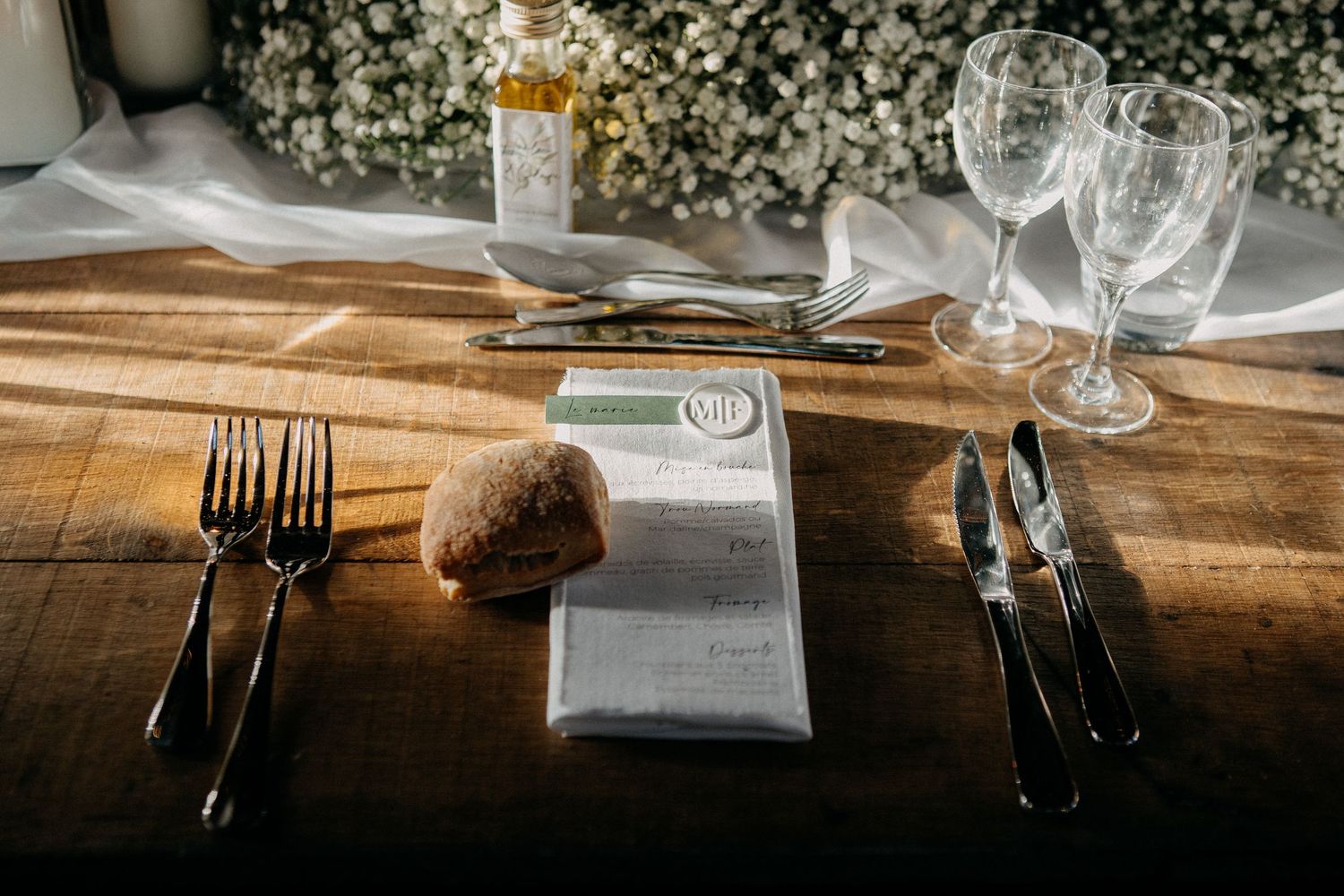 Rustic wooden wedding place setting with menu card, bread roll, and crystal glassware.