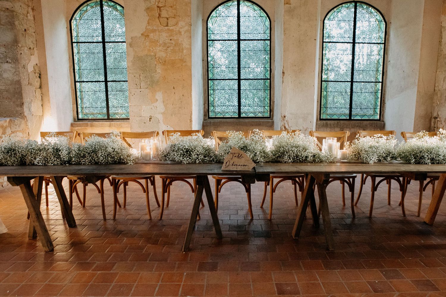 Elegant wedding table setup with baby's breath arrangements and candles beneath arched stone windows.