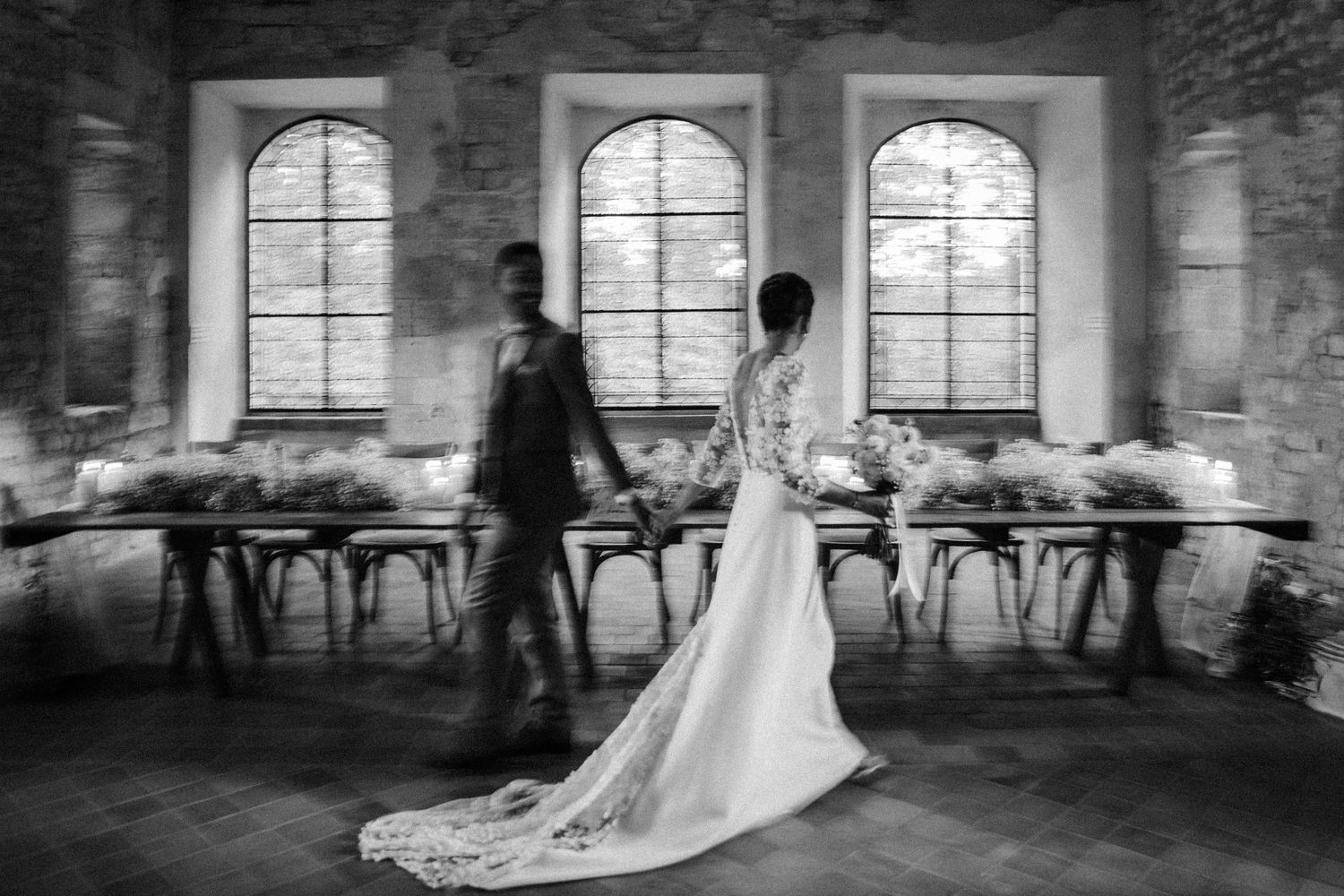 Black and white photo of bride and groom entering rustic stone wedding reception hall.