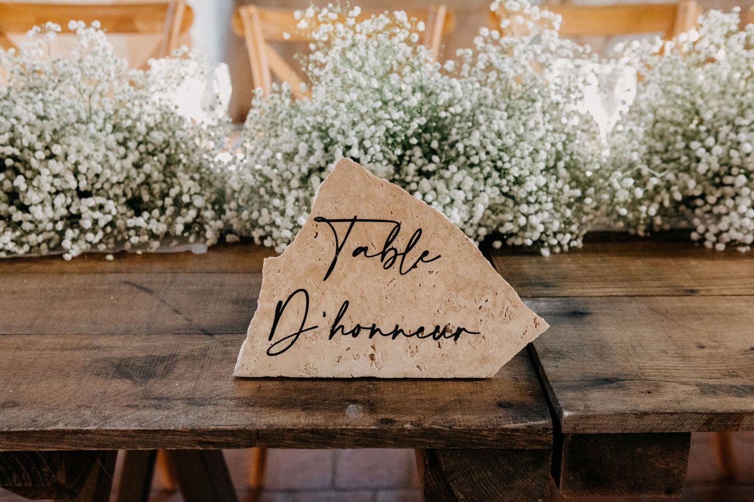 Wooden table number sign reading Table D'honneur surrounded by baby's breath floral arrangements.