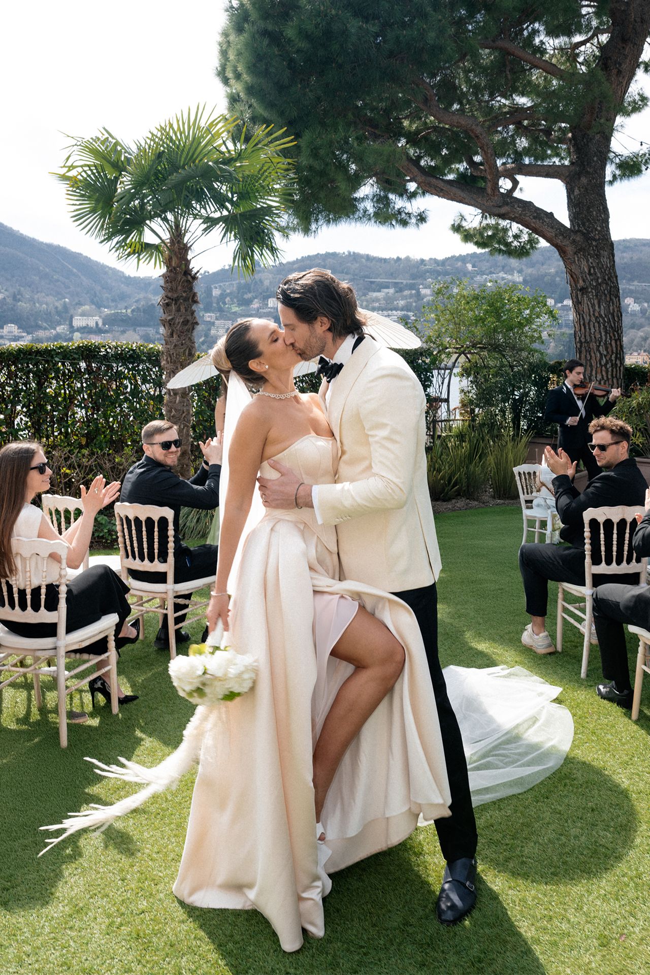 Romantic wedding couple shares intimate moments during outdoor ceremony with white chairs and scenic mountain backdrop.