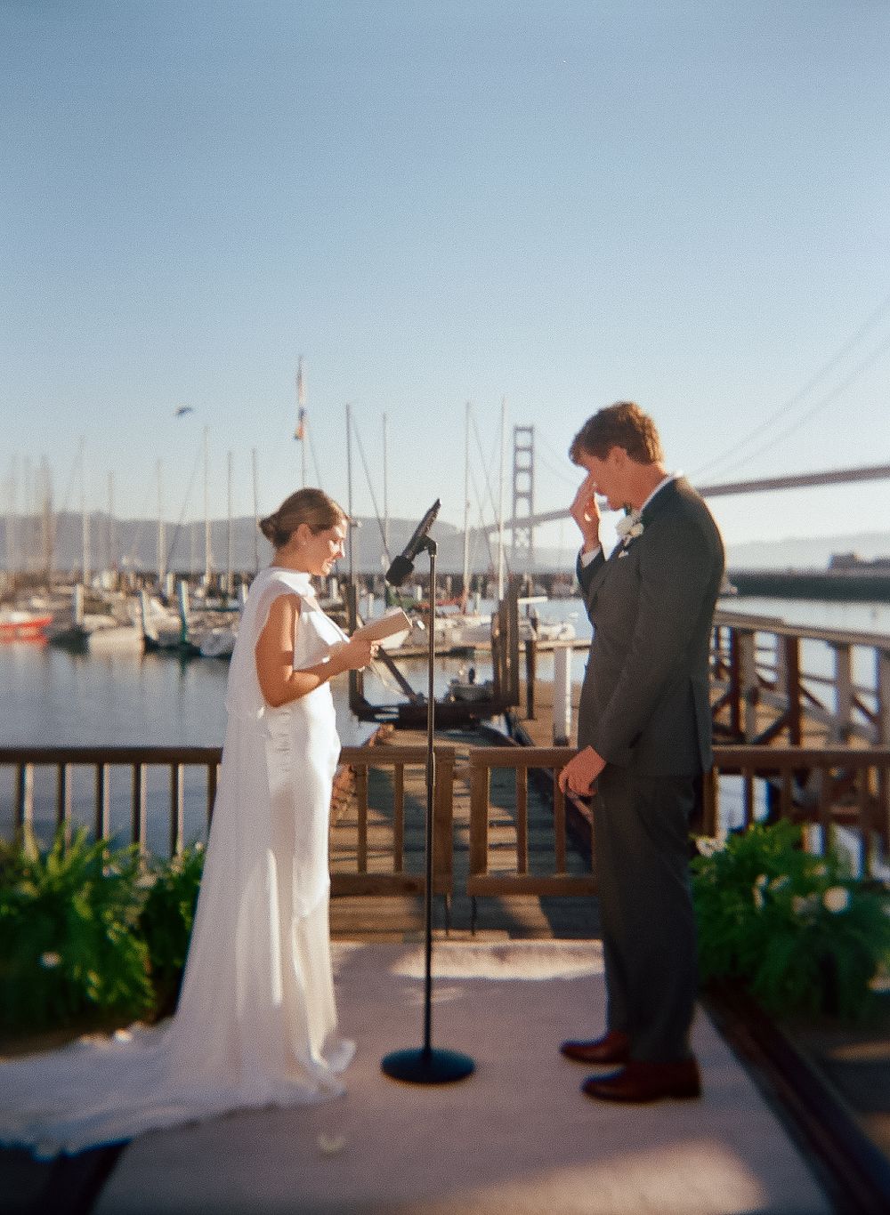 Wedding couple poses playfully with toy guns on a waterfront deck with the Golden Gate Bridge in background.