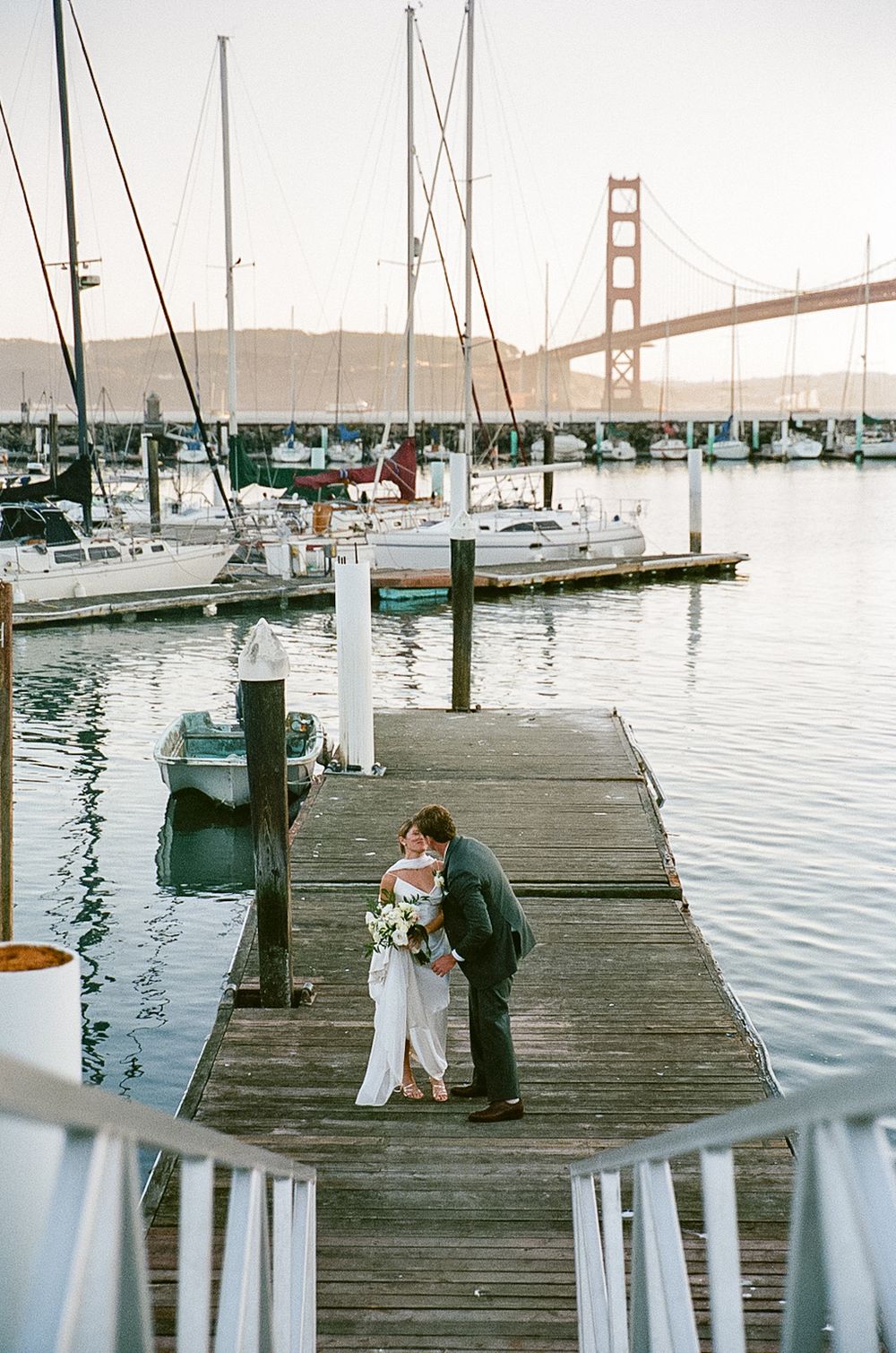 Romantic wedding photoshoot on a wooden pier with San Francisco Bay and Golden Gate Bridge views.