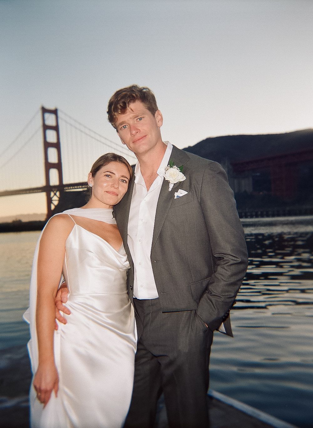 Wedding couple poses romantically at sunset with the Golden Gate Bridge visible in the background.