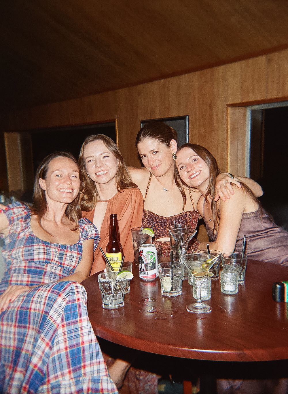 Friends gather around a wooden table with mason jar drinks at a casual celebration.