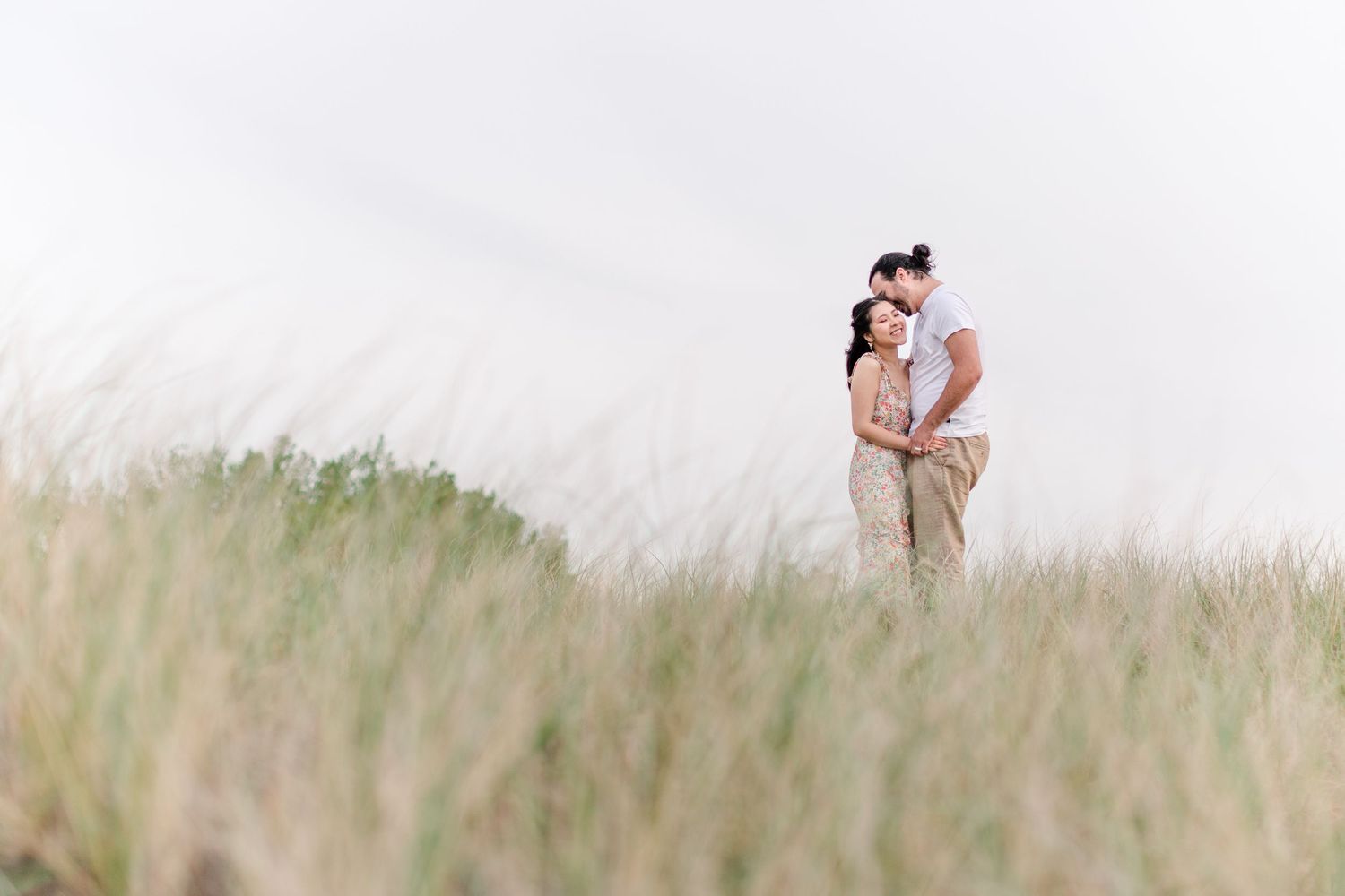 A couple embracing in a serene field of tall grass during golden hour.