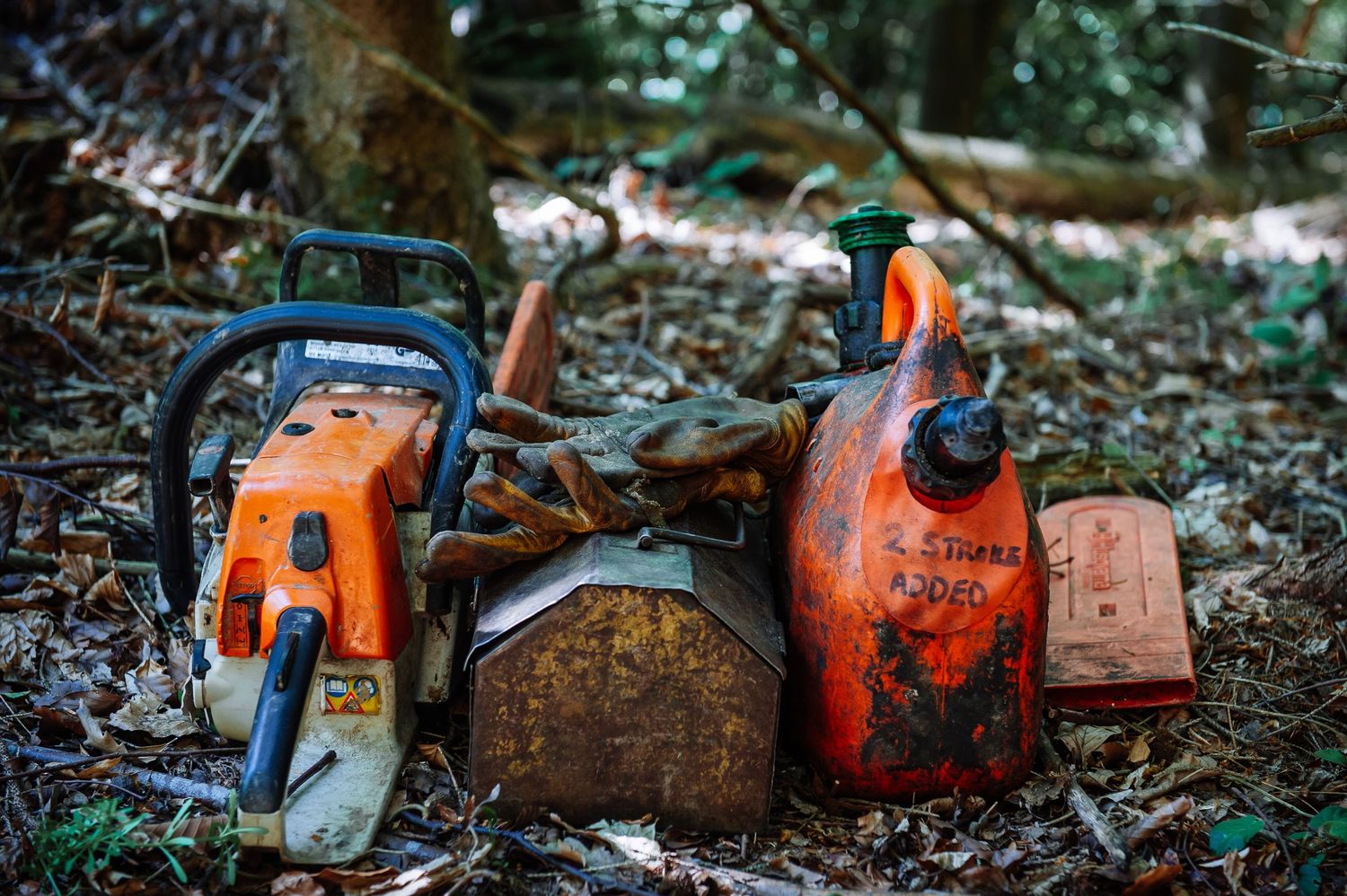 Collection of used chainsaws and forestry equipment scattered on forest ground.