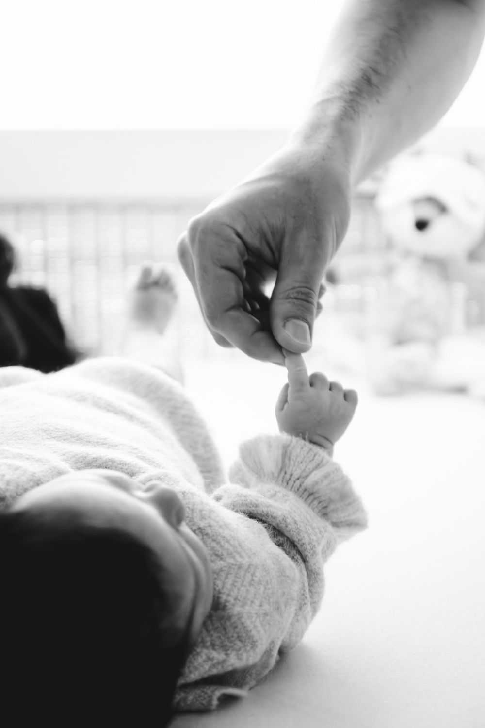 Black and white photo of a newborn baby grasping an adult finger in a nursery.