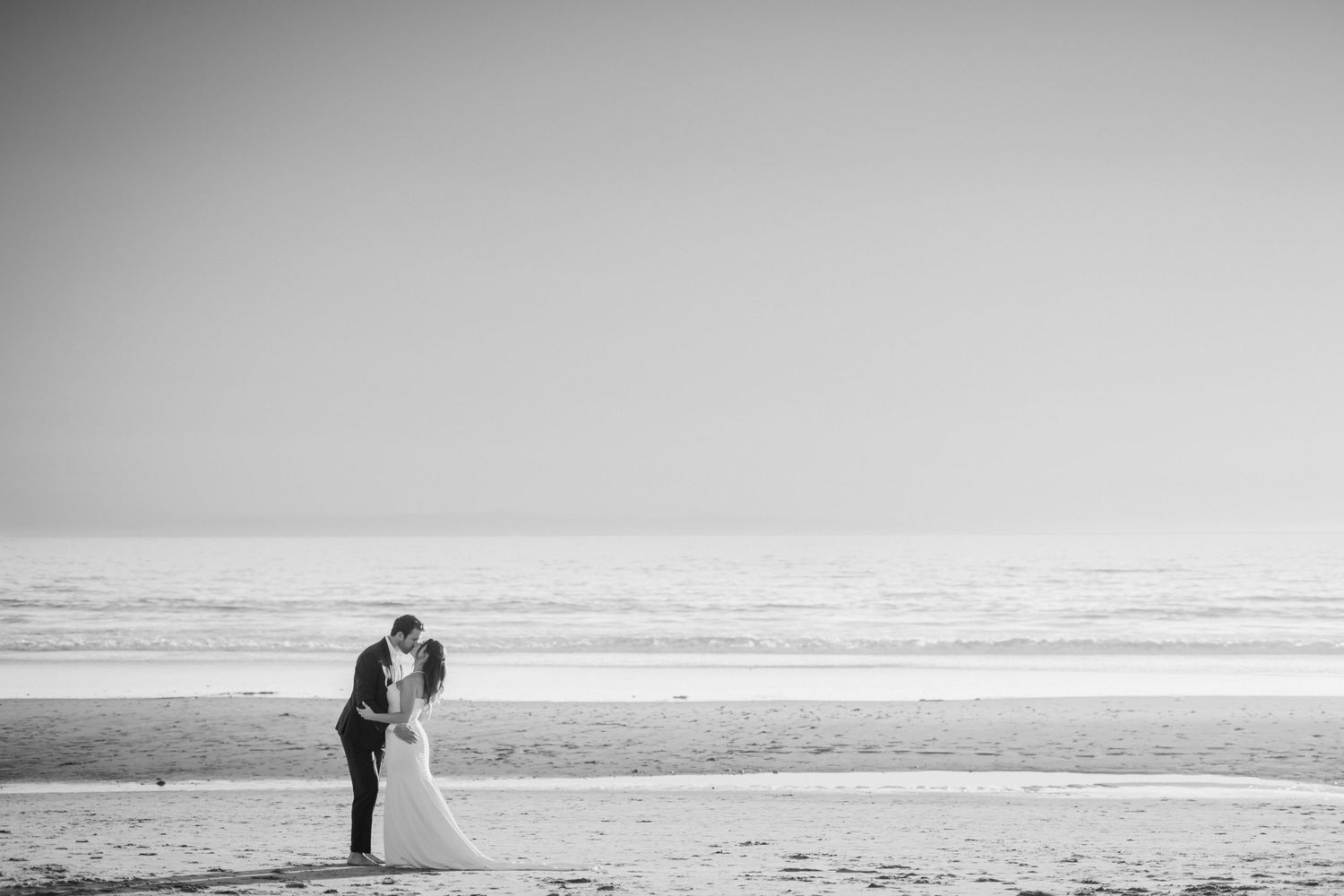Silhouettes of a wedding couple walking along a misty beach at sunset.