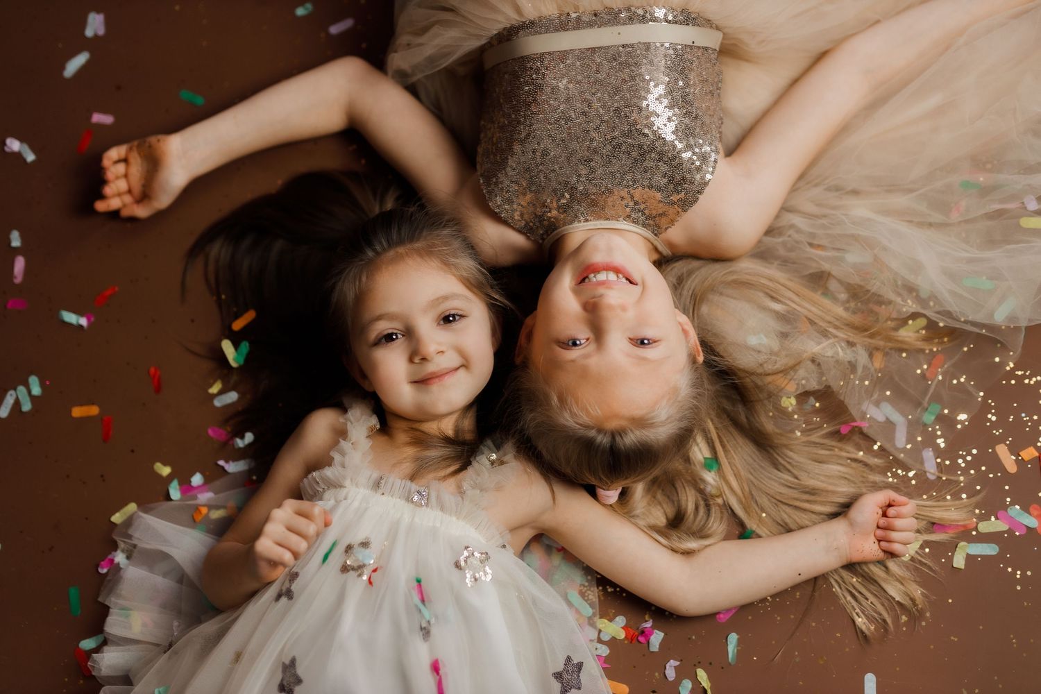 Colorful sprinkles and confetti being scattered across a pink surface with hands visible in the frame.