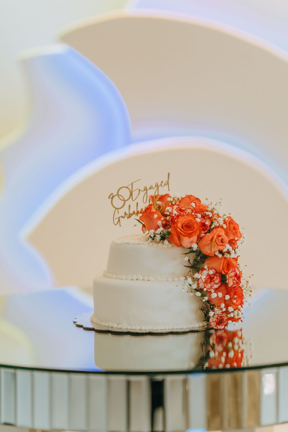 A white wedding cake decorated with cascading orange flowers on a glass table.