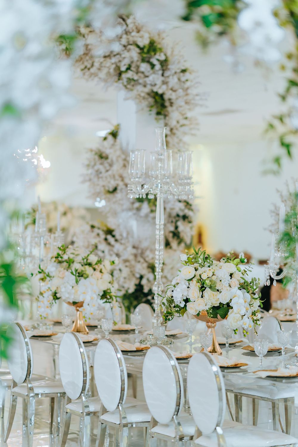 Elegant wedding reception table setting with crystal glasses and white floral arrangements in a bright space.