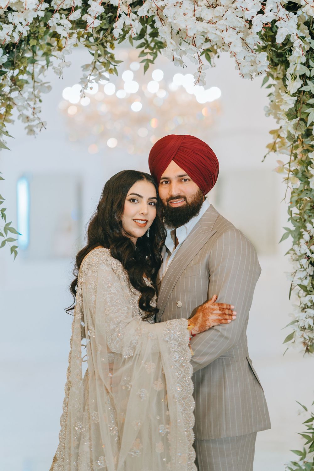 A couple shares a joyful moment during their Sikh wedding ceremony under hanging floral decor.