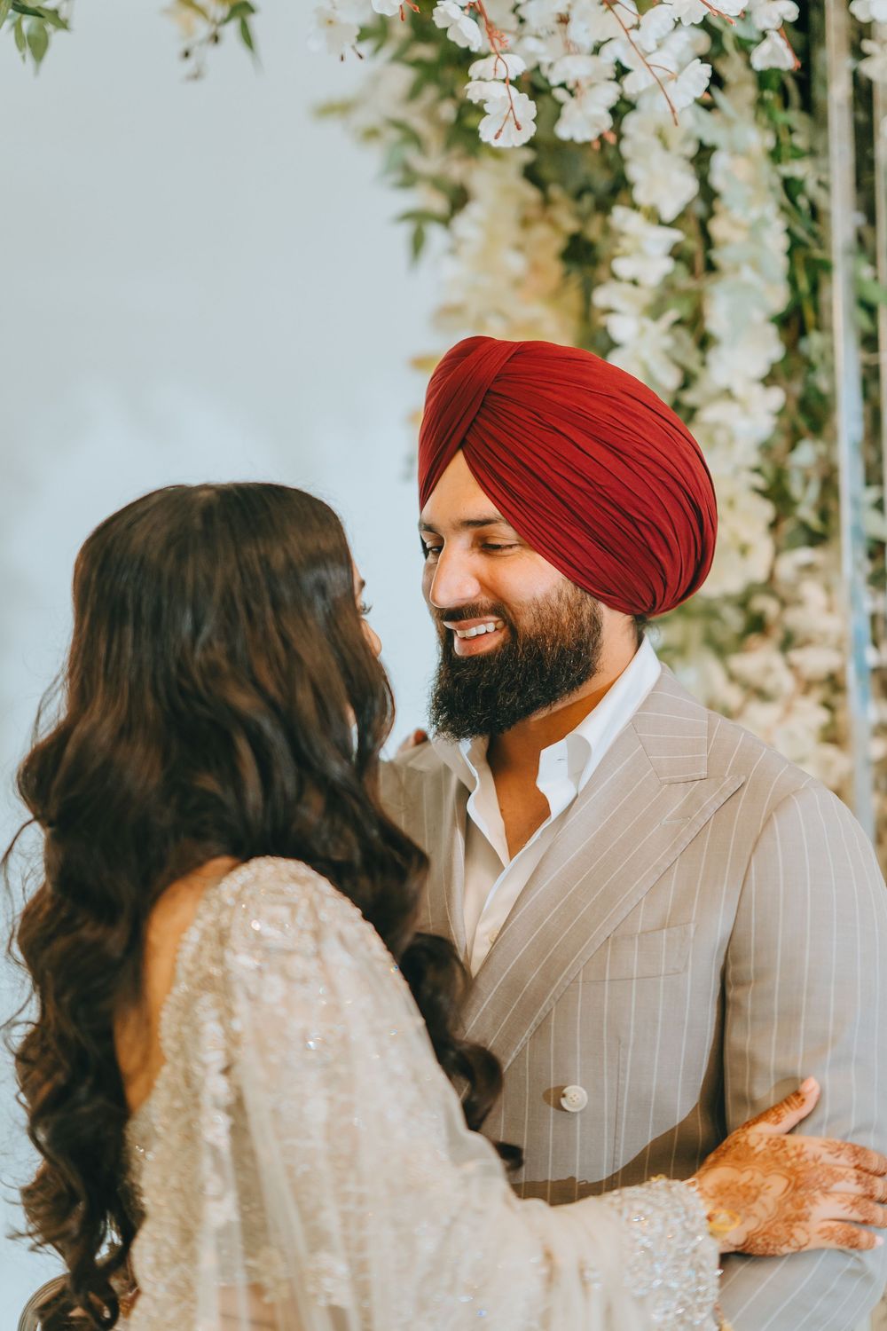 A couple in traditional Sikh wedding attire shares an intimate moment under white floral decorations.